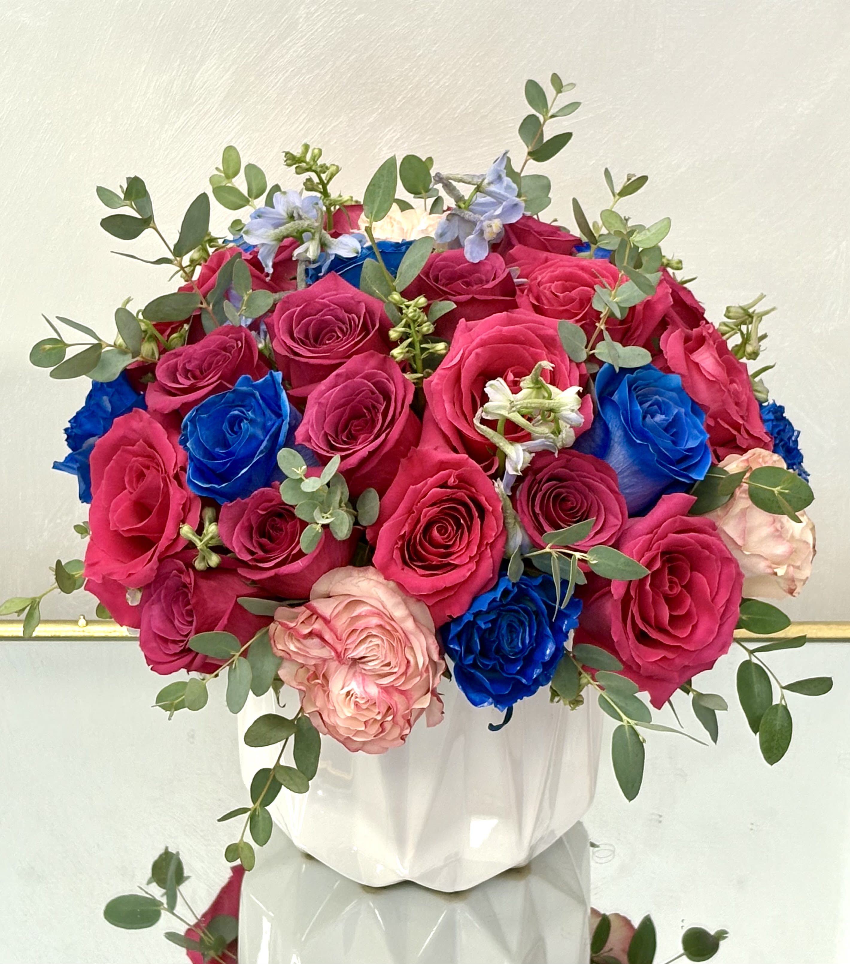 Bouquet of pink, blue, and blush roses in a white vase
