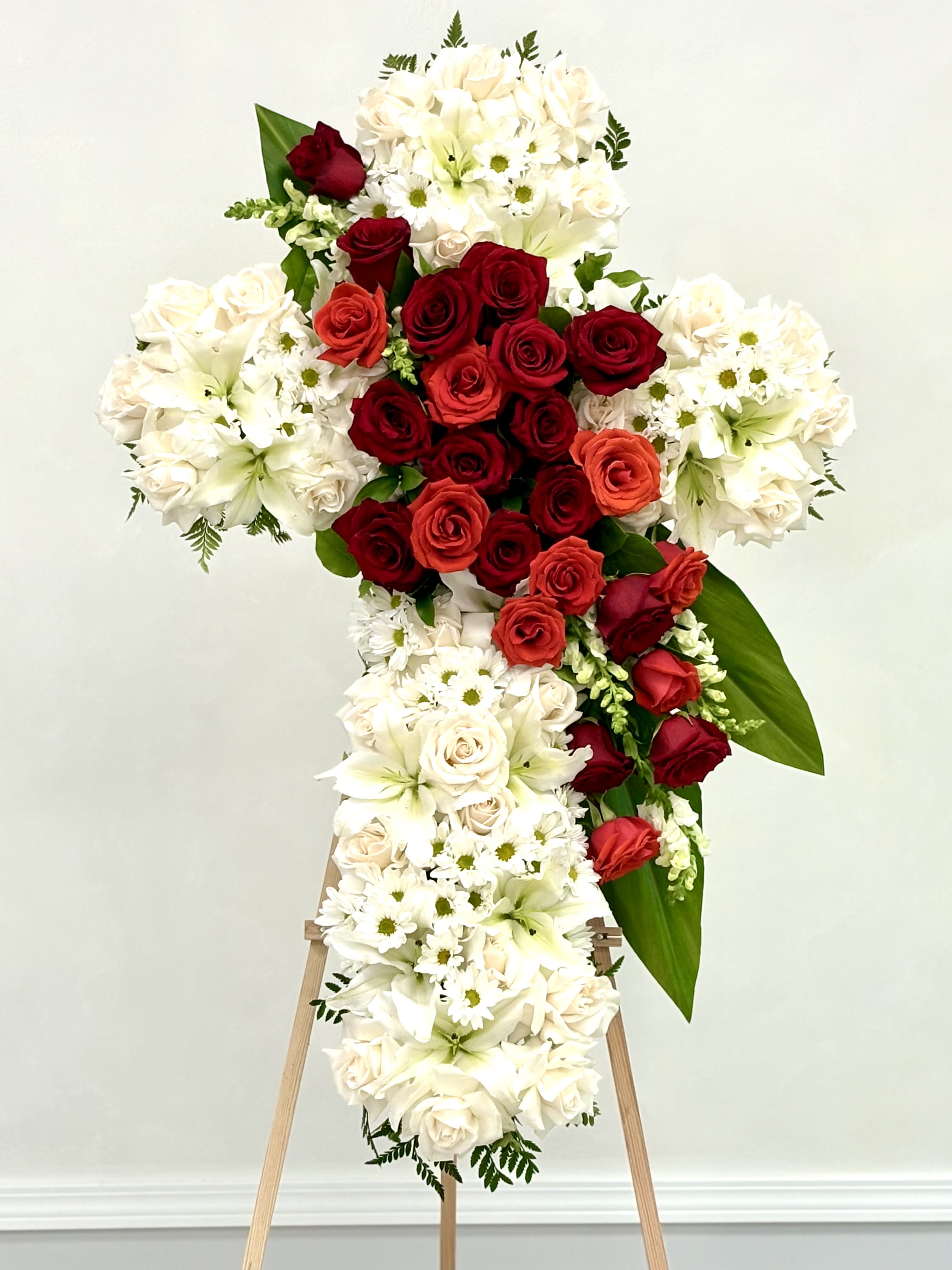 Standing floral cross with red and white roses and lilies on an easel