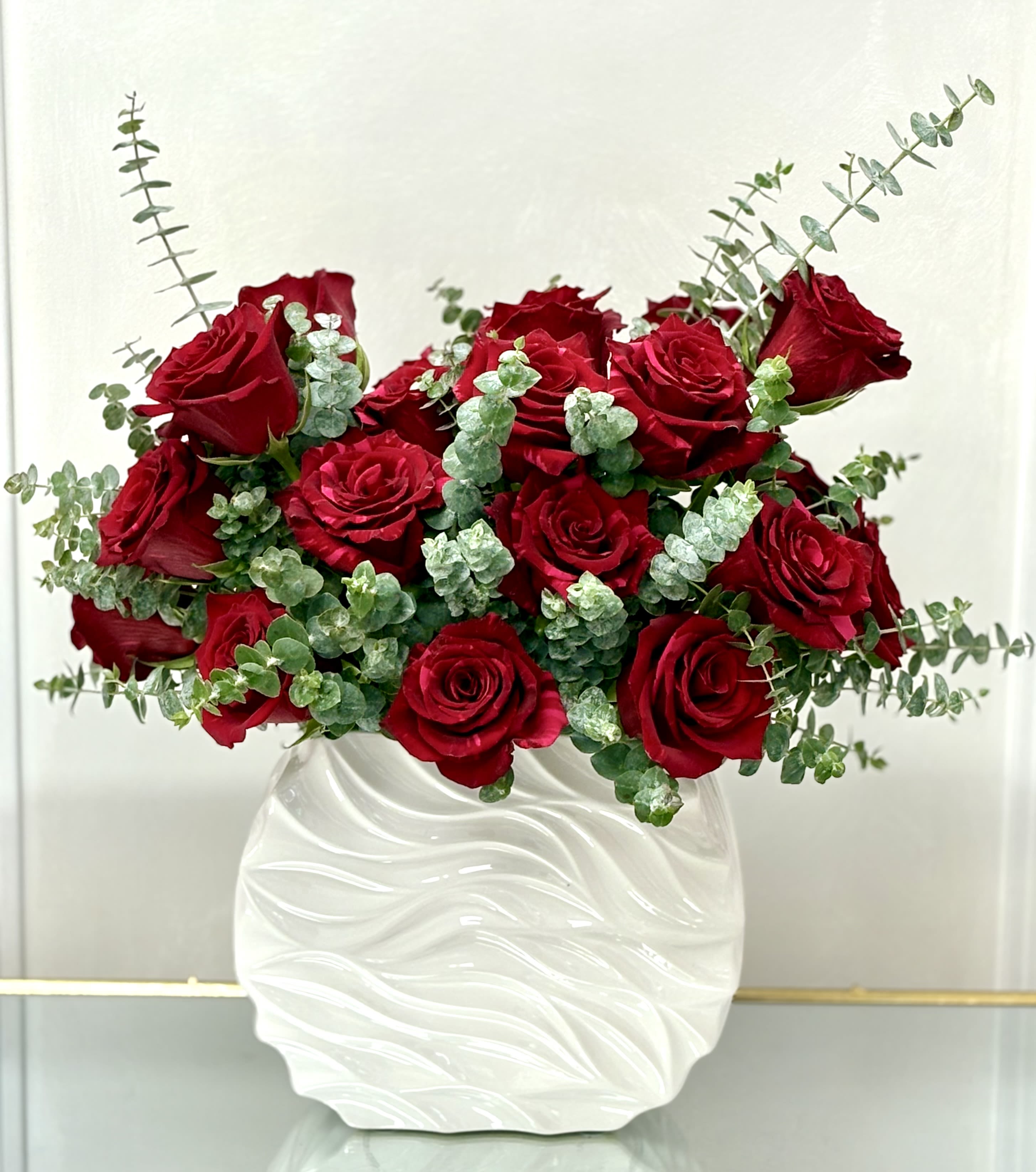 Arrangement of red roses and eucalyptus in a textured white ceramic vase