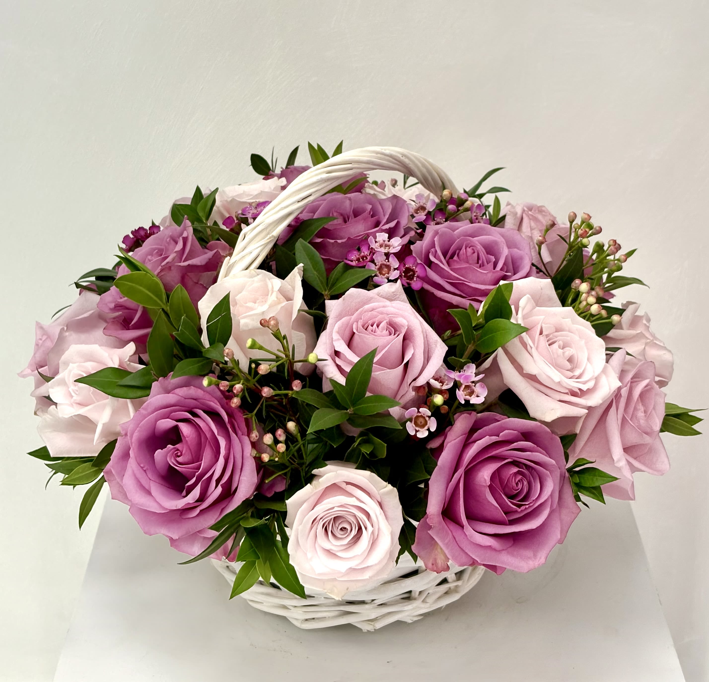 Basket of pink and lavender roses with small filler flowers