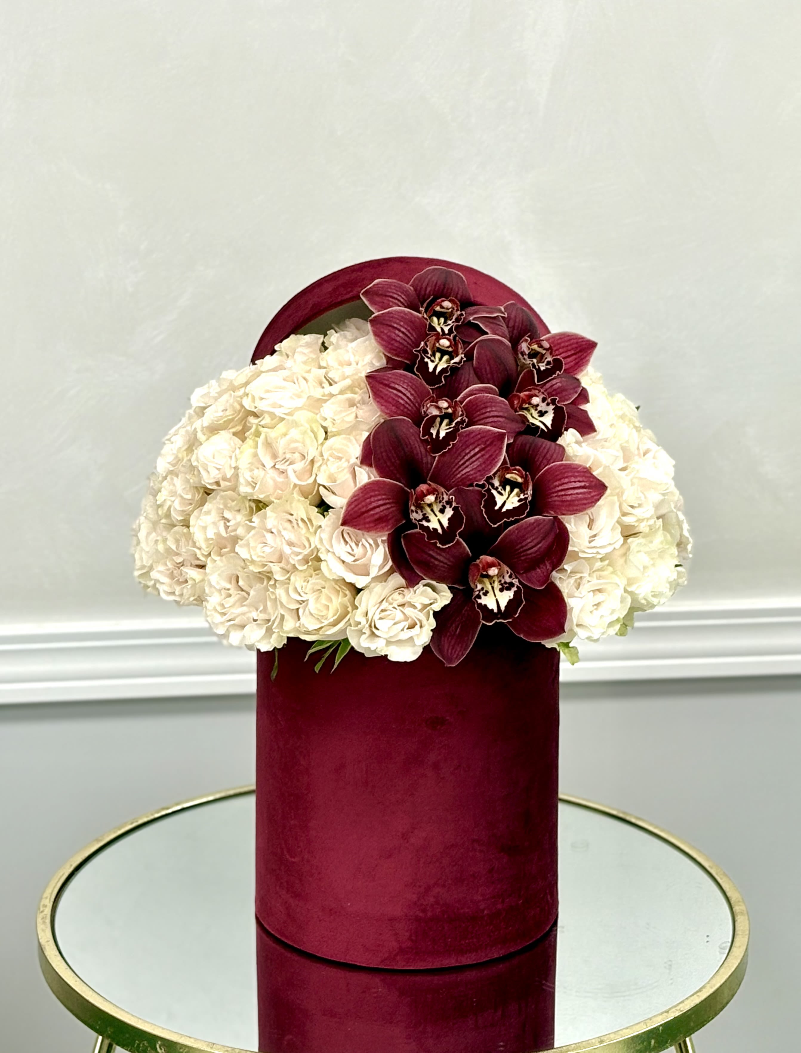Cream hydrangeas and burgundy orchids in a velvet hat box