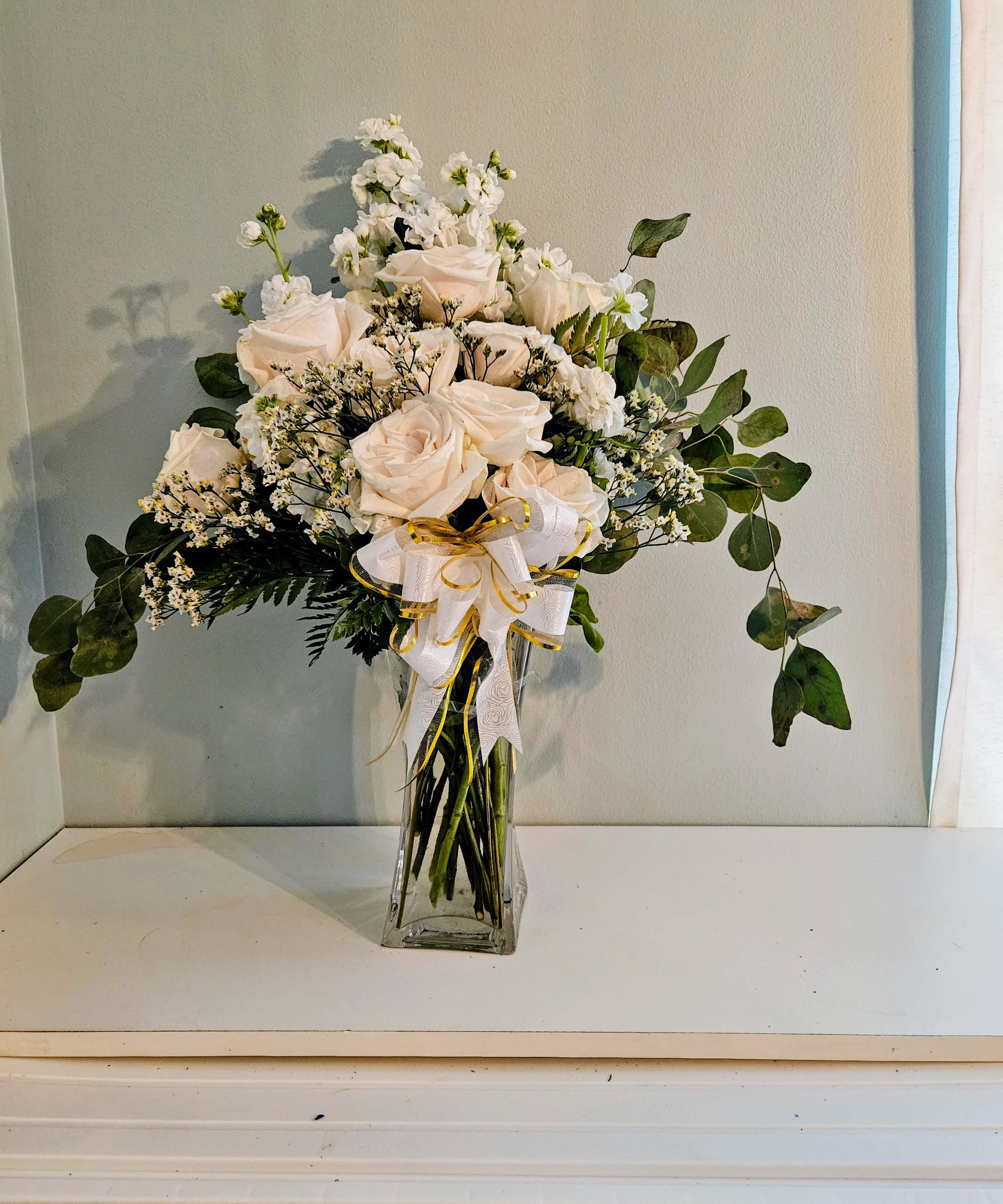 White roses and small white flowers in a clear glass vase with a ribbon