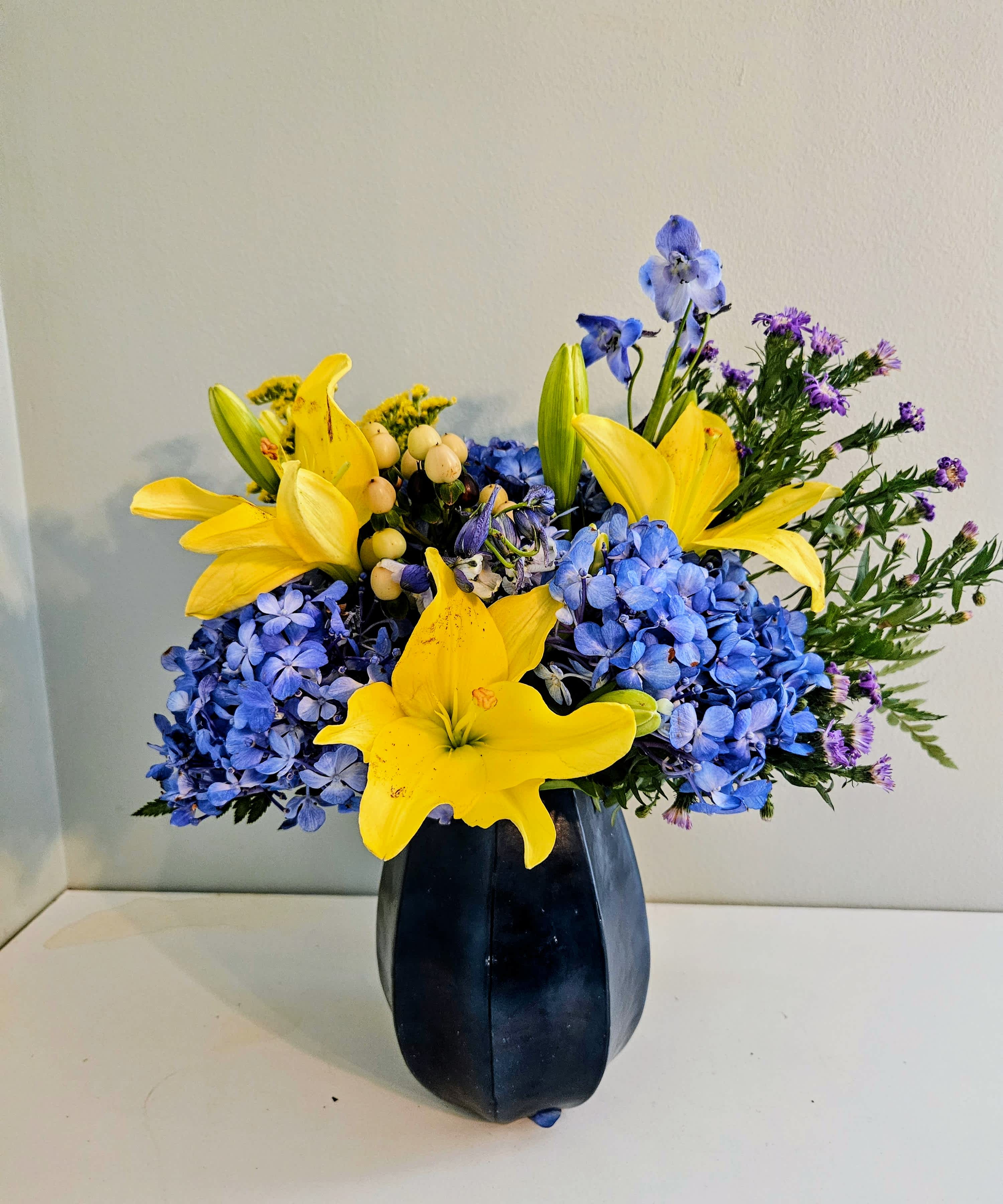 Blue hydrangeas and yellow lilies arranged in a dark vase