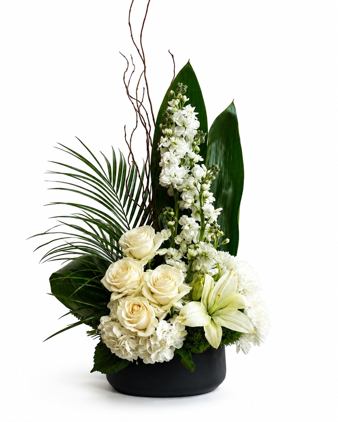 White roses, lilies, and tall white blooms in a black vase with large green leaves