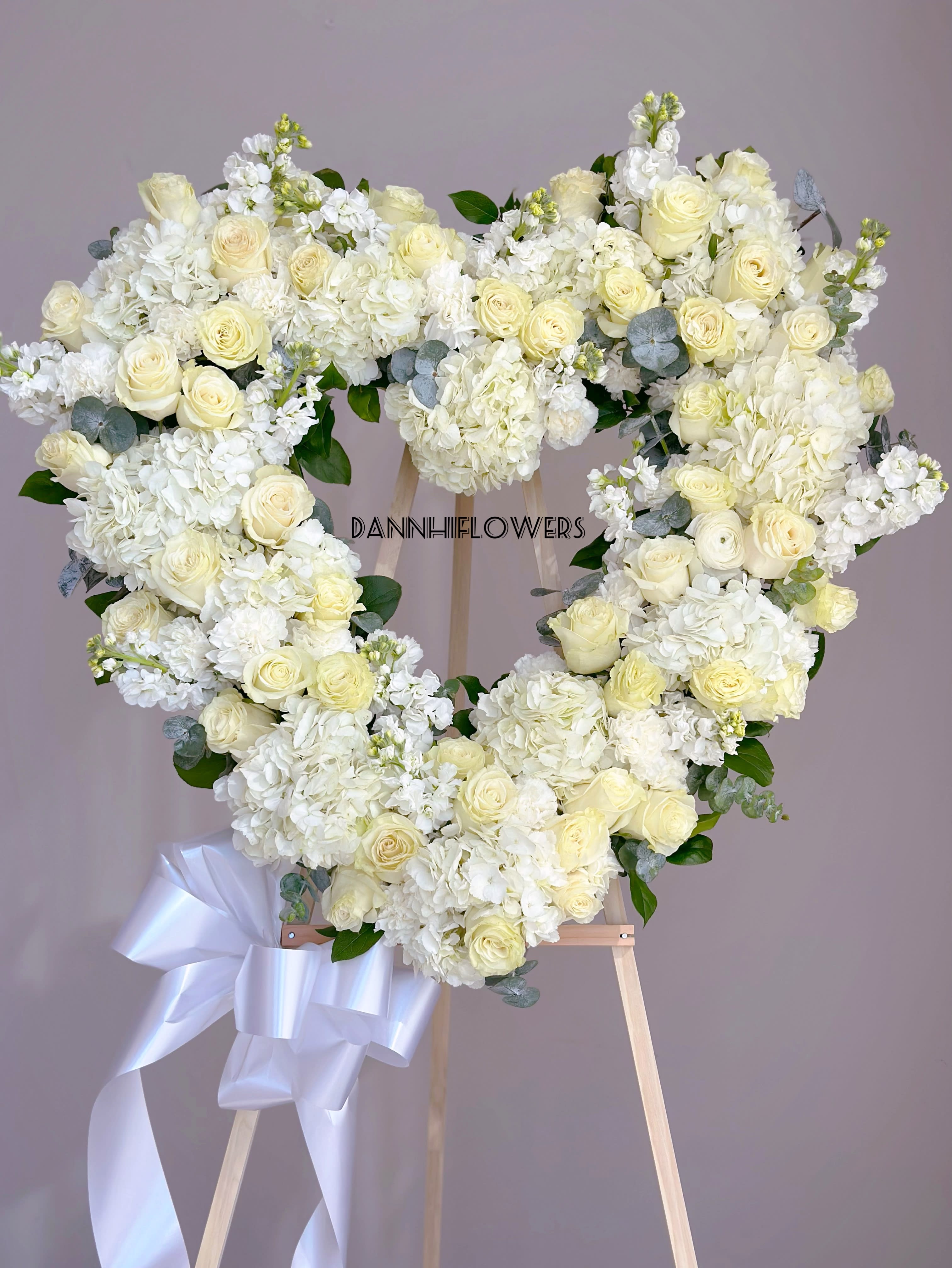 Heart-shaped white floral wreath on an easel with a ribbon bow
