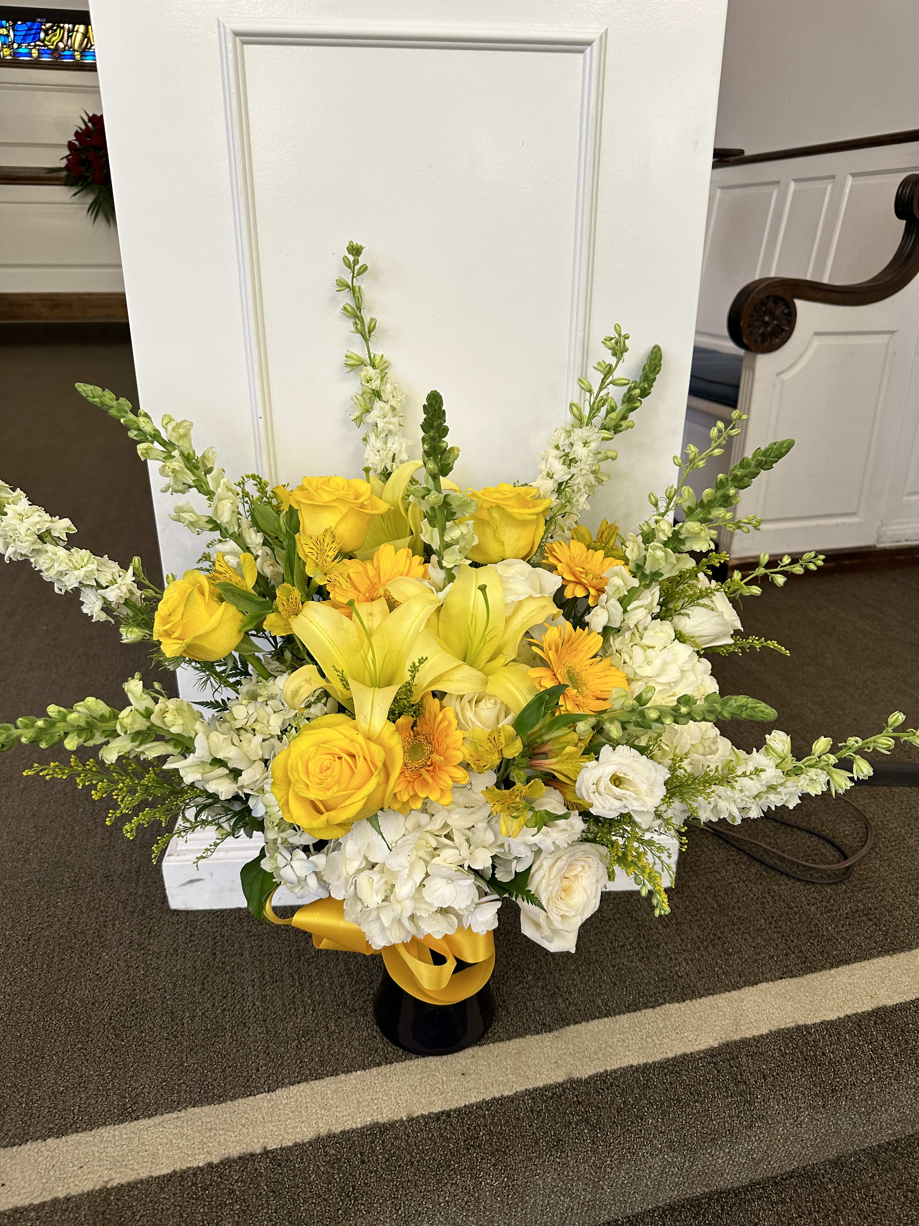 Yellow and white floral arrangement in a black vase with a yellow ribbon