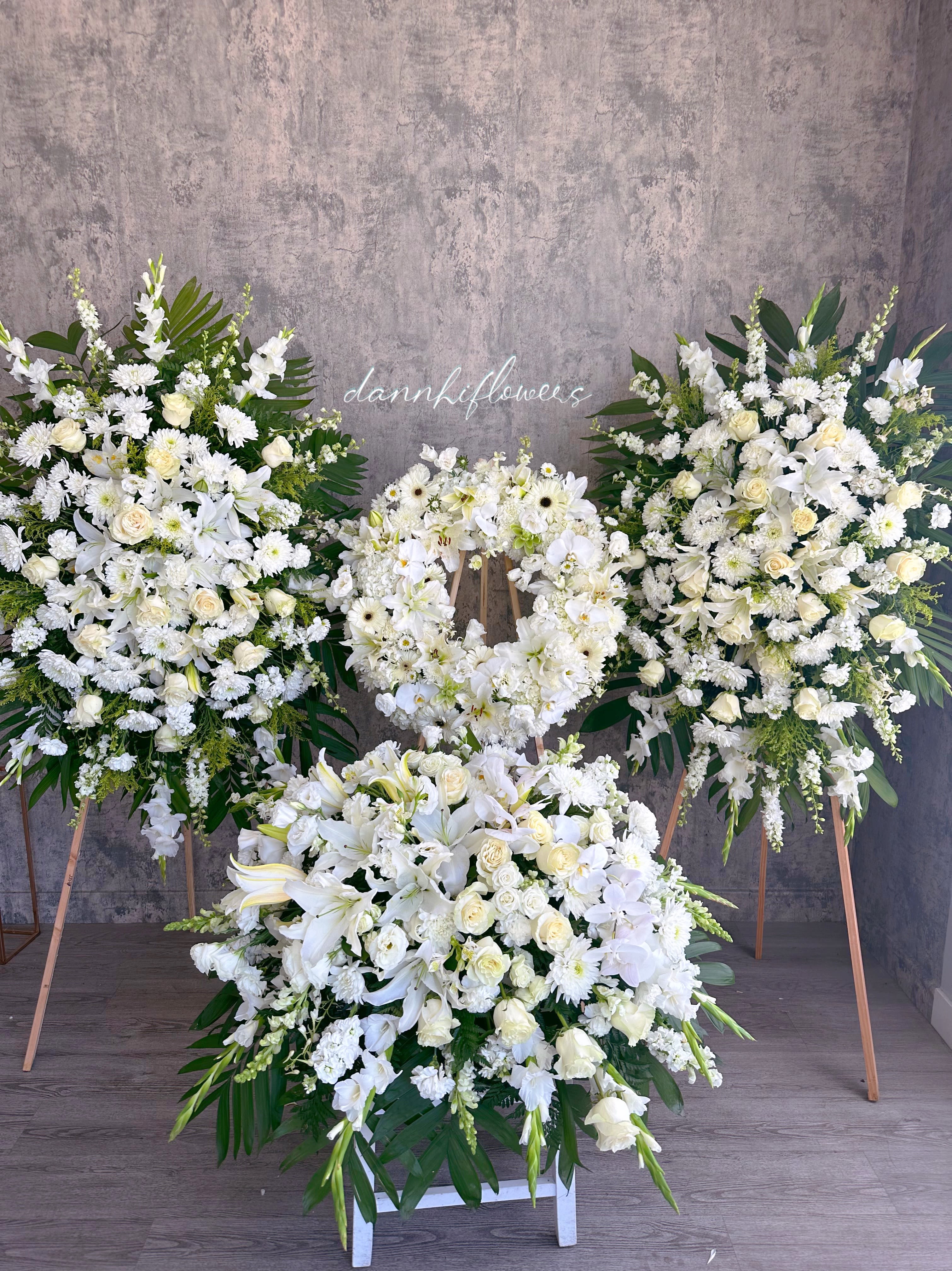 White floral funeral wreaths and sprays on stands with a large floor arrangement