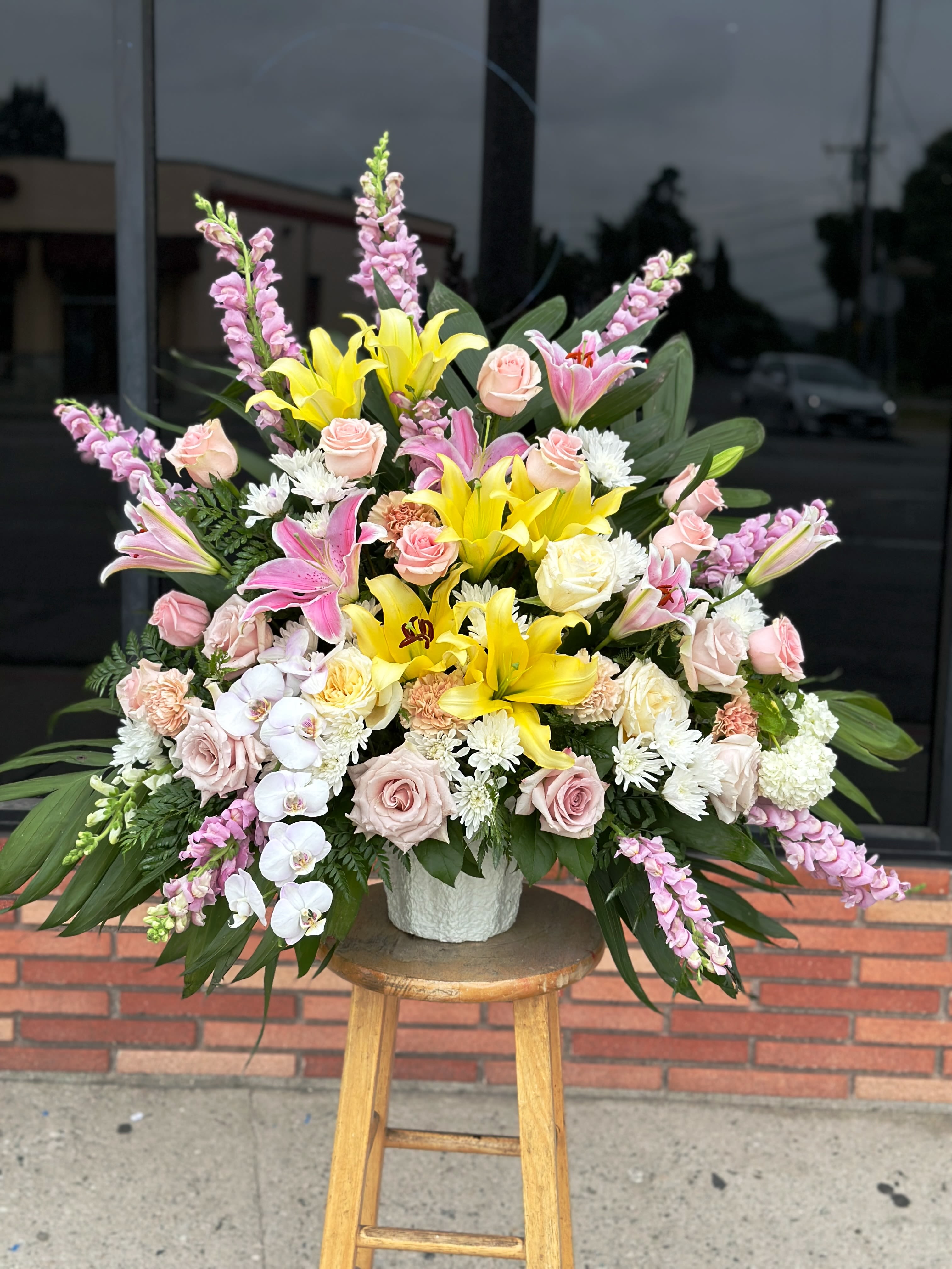 Large mixed bouquet with yellow lilies, pink roses, and orchids in a white vase