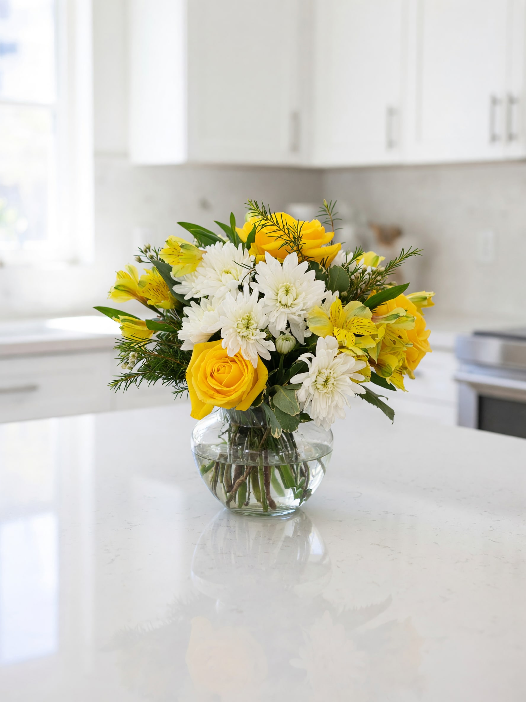 Yellow roses and white daisies in a clear glass vase