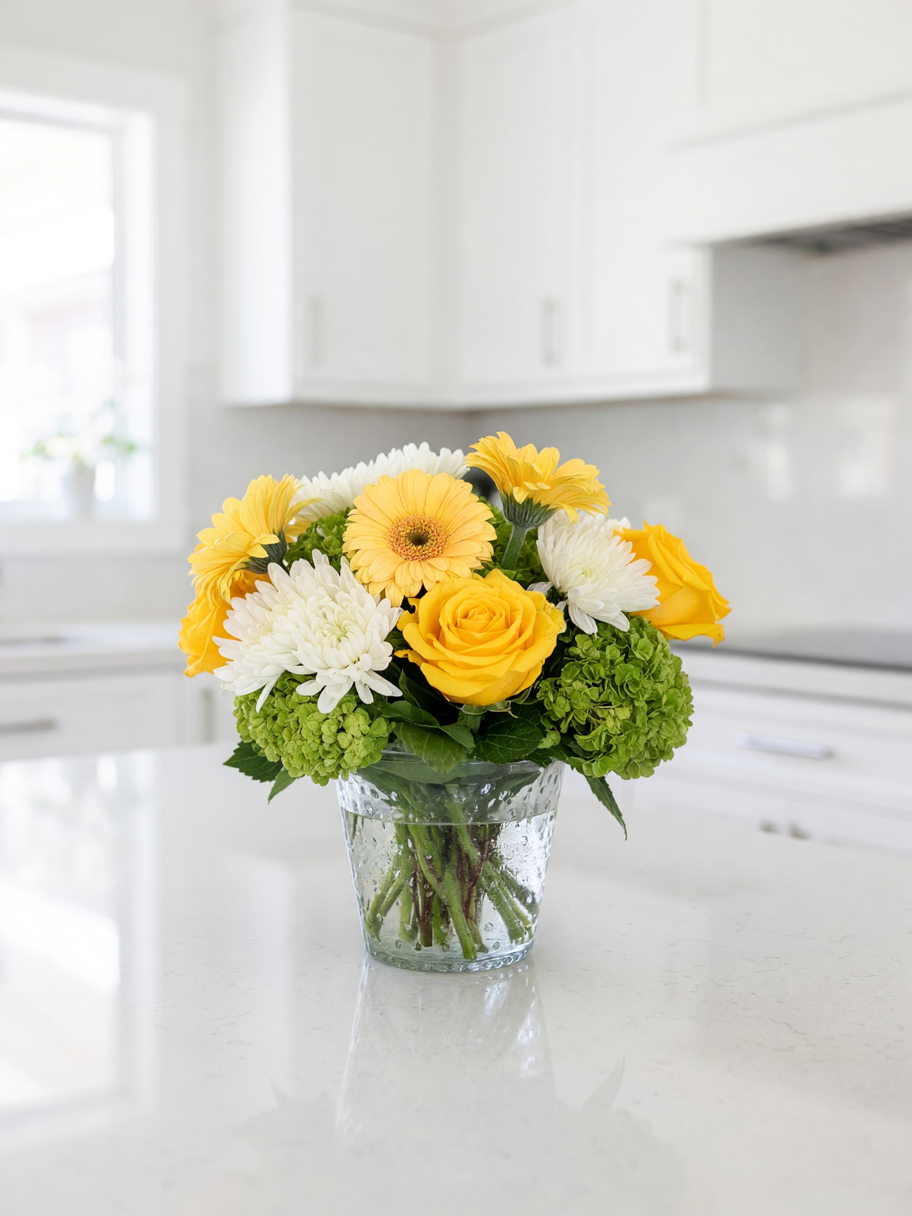 Yellow and white flowers arranged in a clear glass vase