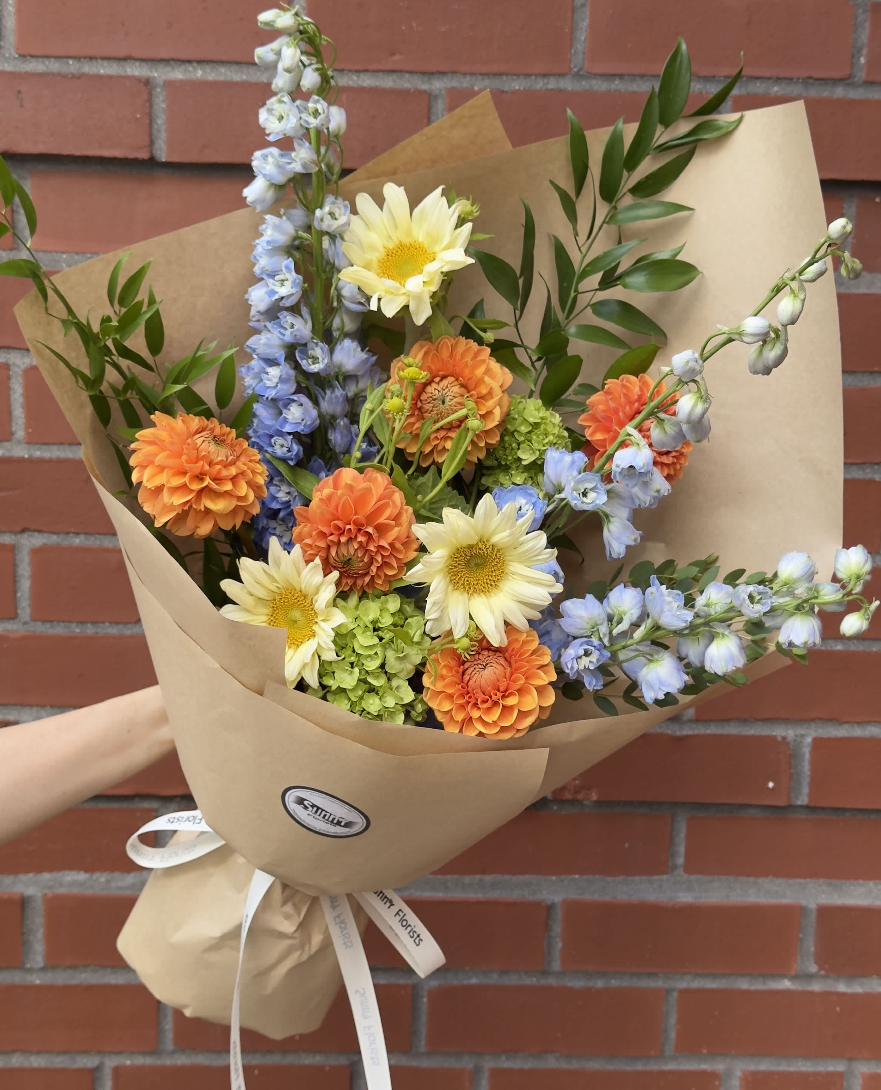 Bouquet of orange and pale yellow flowers wrapped in brown paper