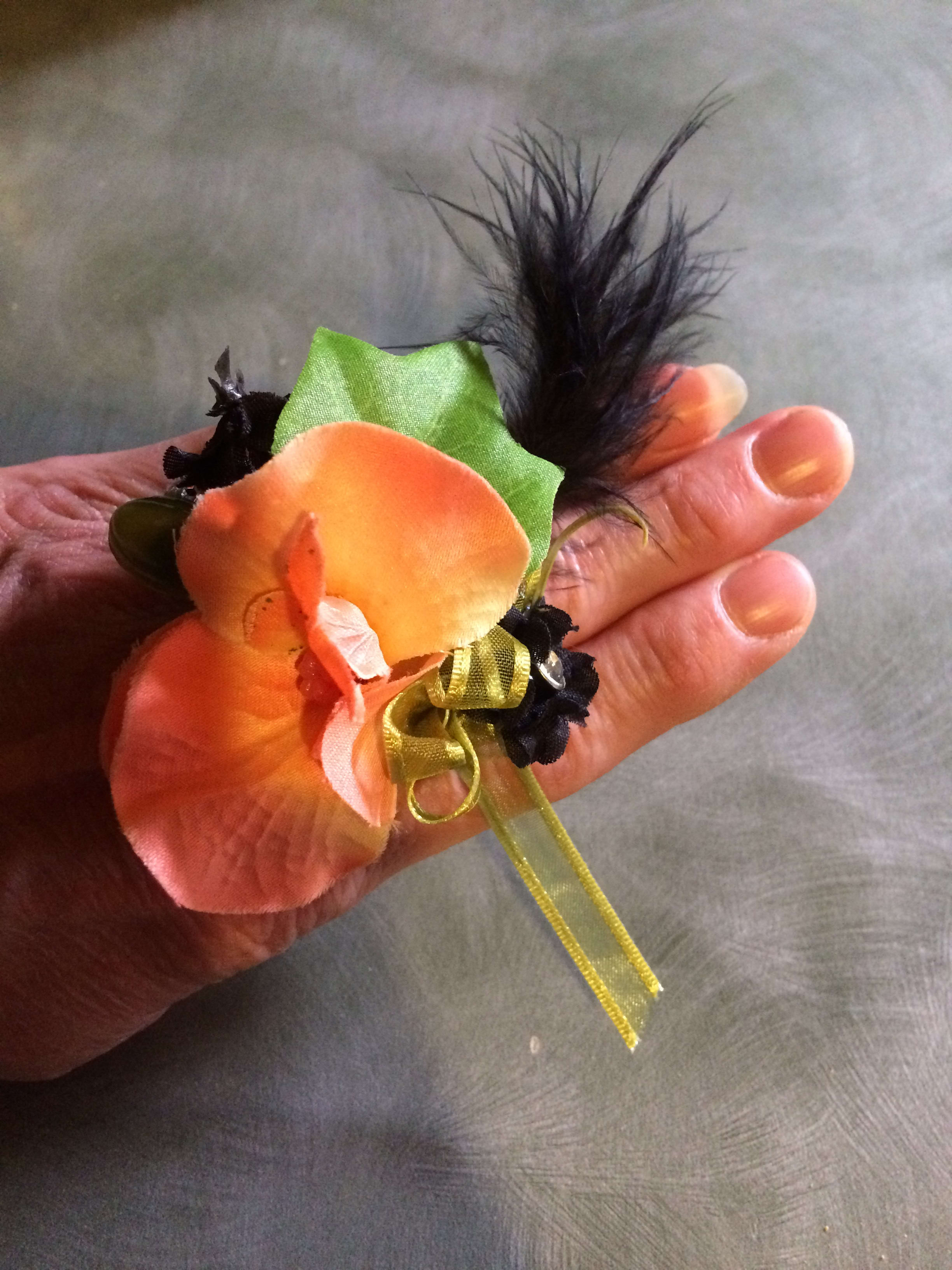 Small orange flower corsage with black feathers and ribbon