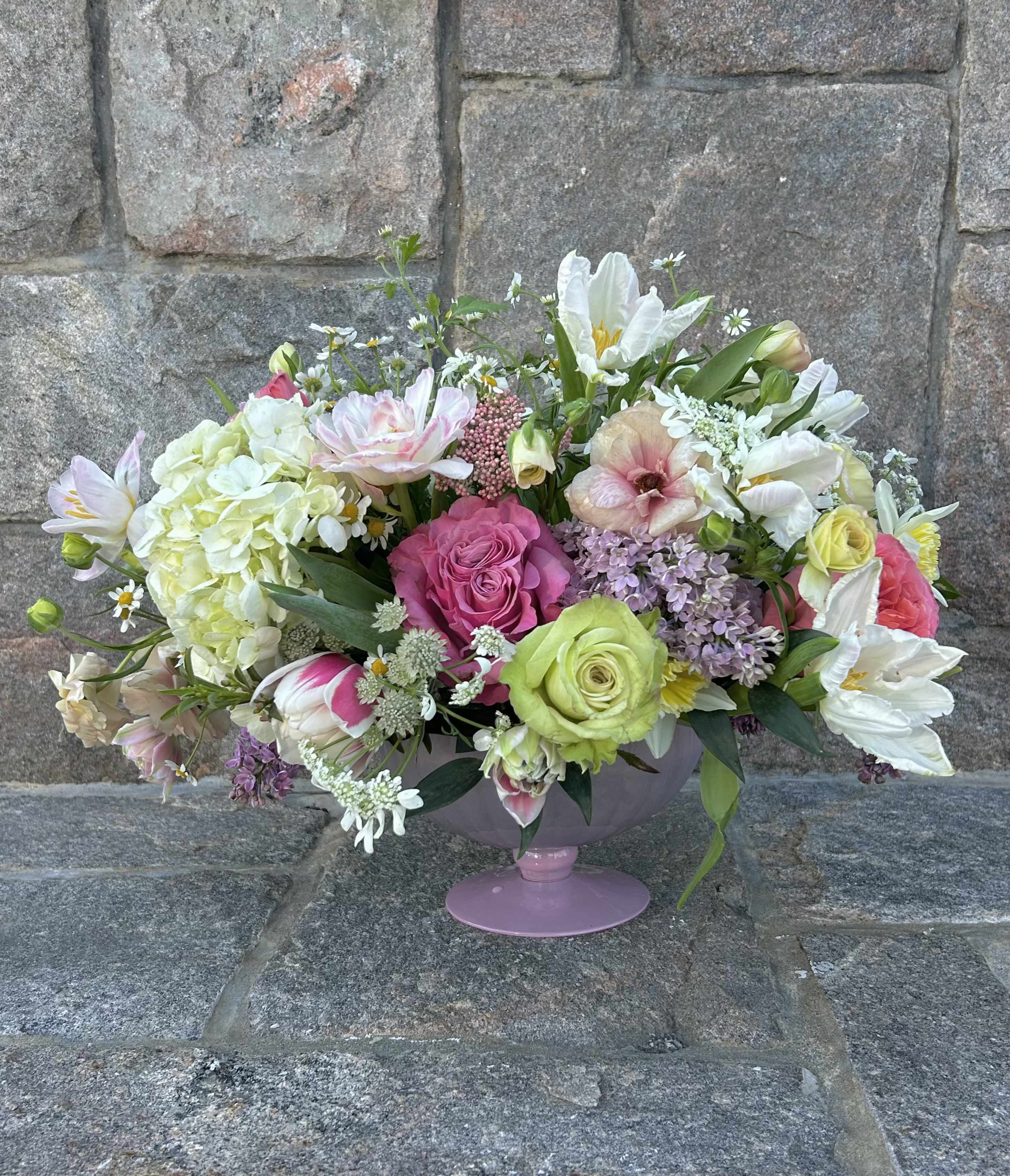 Low pink compote filled with pink roses, white tulips, hydrangeas, and mixed pastel blooms.