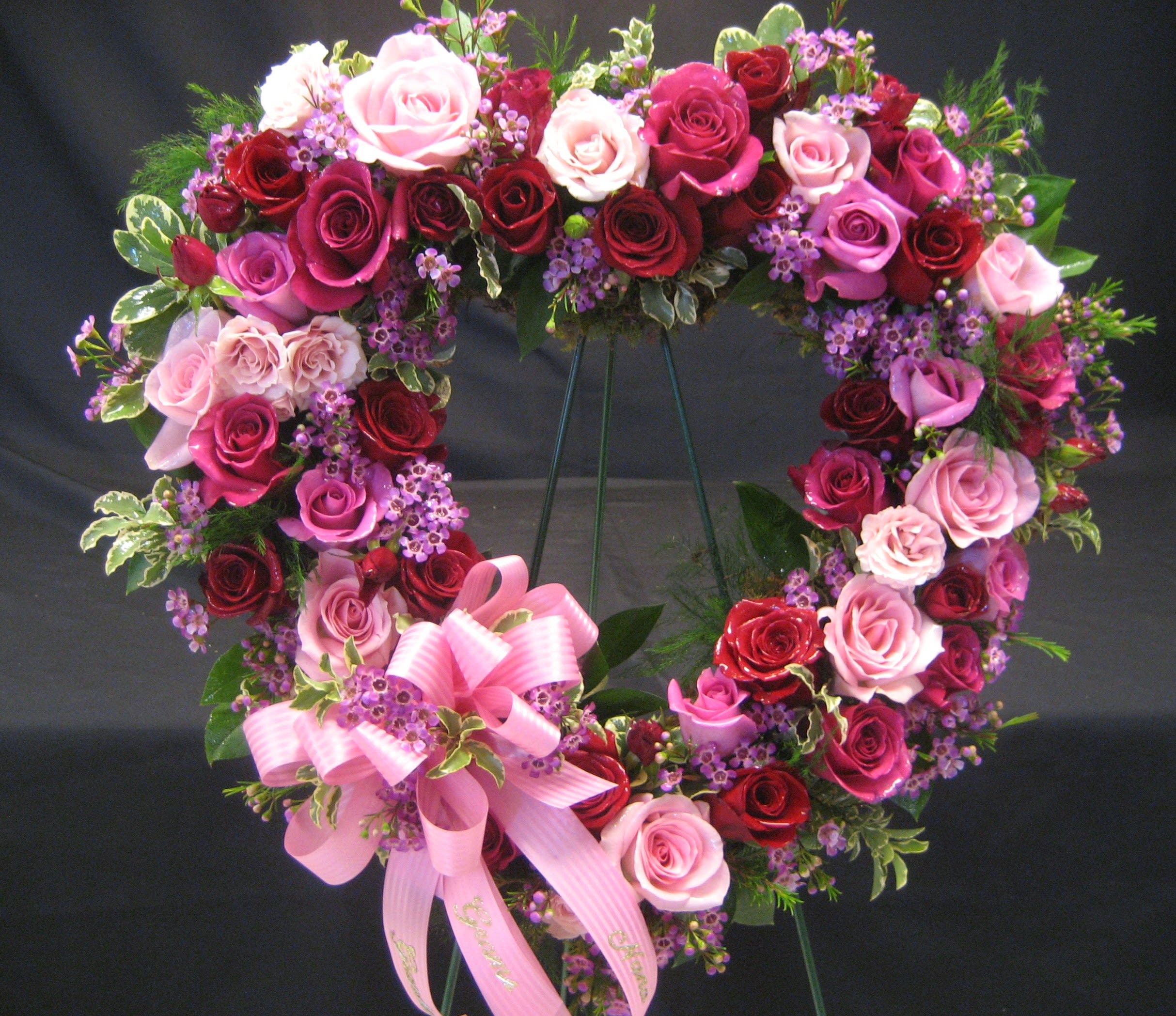 Heart-shaped rose wreath with pink ribbon bow on a stand