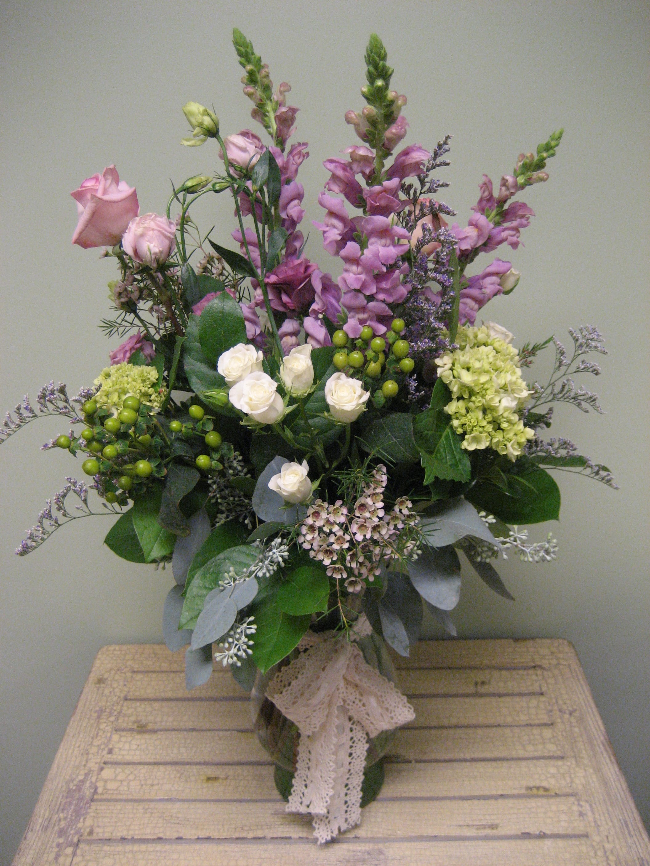 Tall bouquet of pink and white flowers in a glass vase with lace ribbon