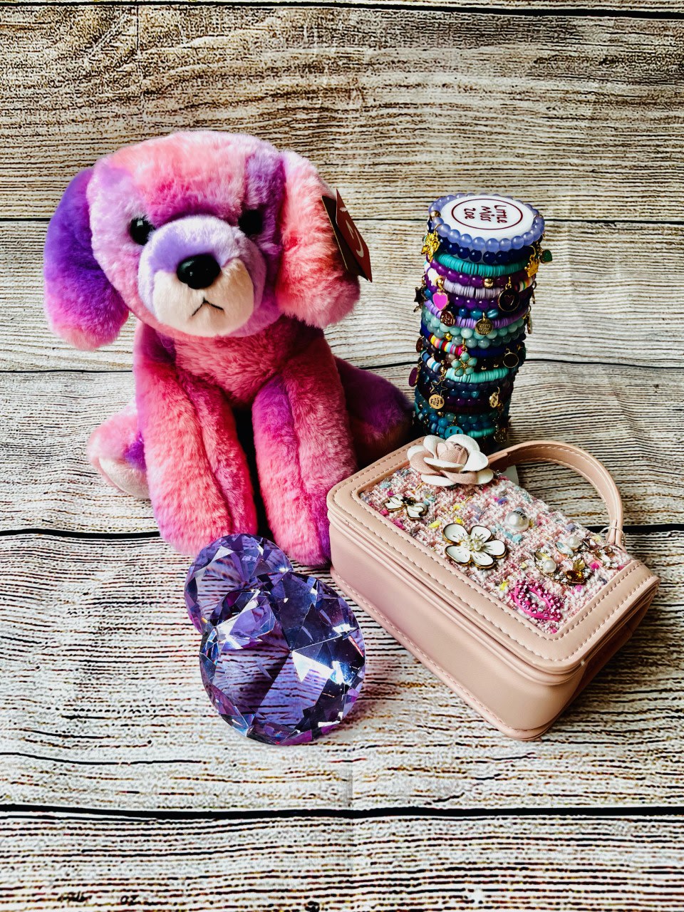 Pink and purple plush dog with a beaded bracelet stack and jeweled case