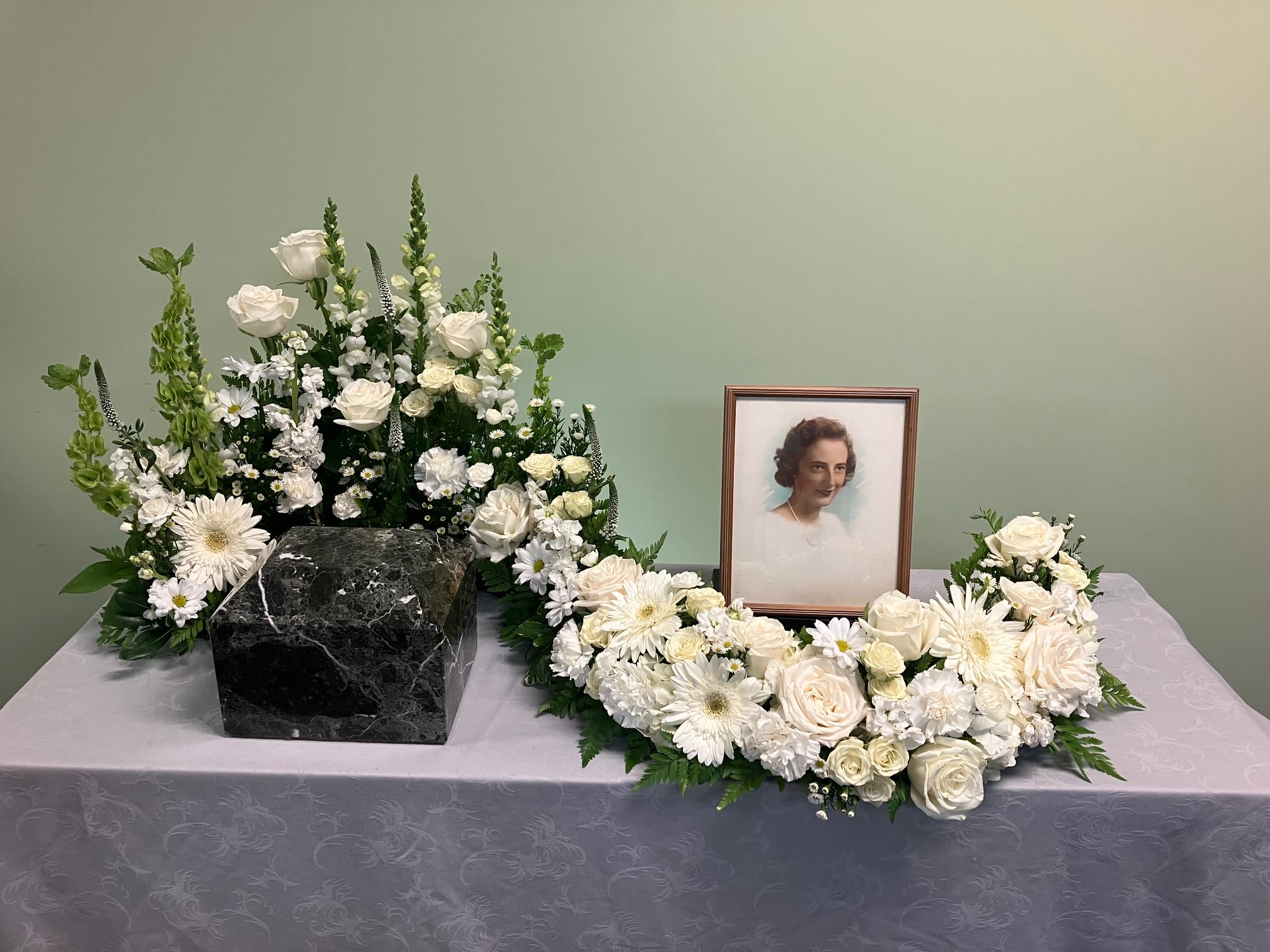 White Urn Serpentine S01 -  This all white Serpentine arrangement is designed to wrap around an urn allowing a tribute to be placed in addition to it . Upgrading to Deluxe or Premium will add more flowers to your design. **Ribbon Script is an additional $10