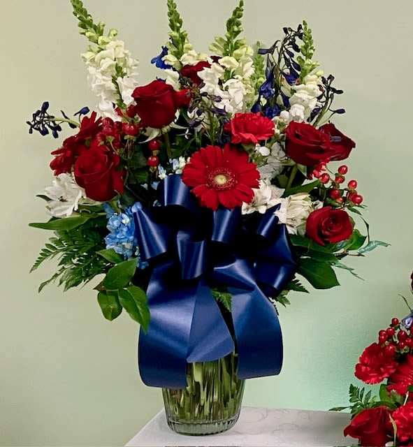 Red roses and white flowers in a glass vase with a blue ribbon