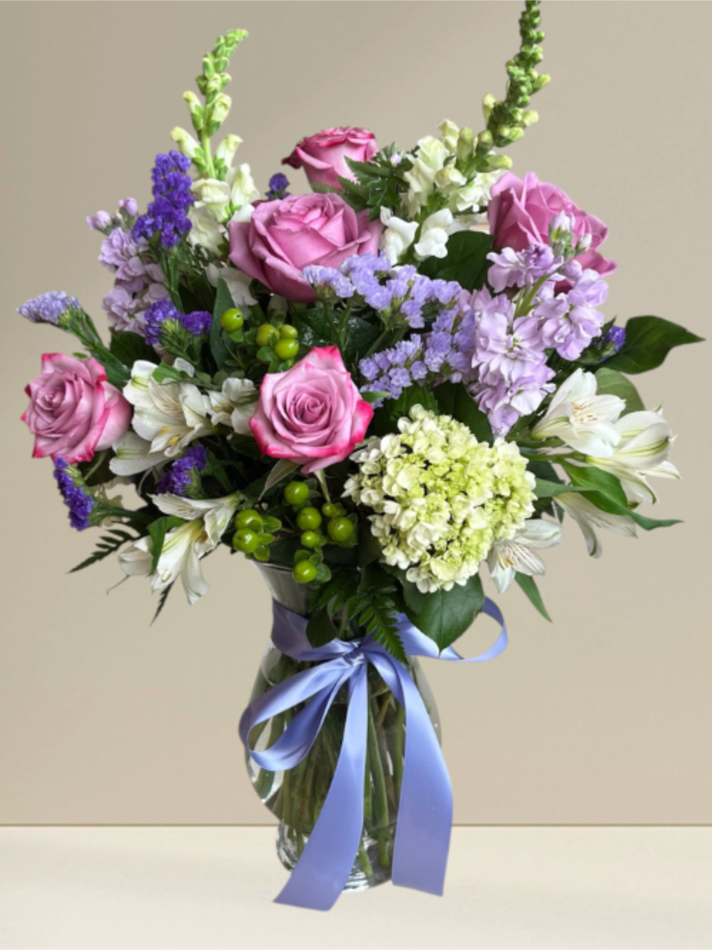 ED11 Lavender Wish  - This tall showy clear glass vase is a mix of lavender and white flowers accented with a satin bow. Upgrading to a Deluxe or Premium arrangement will add more blooms to the design.