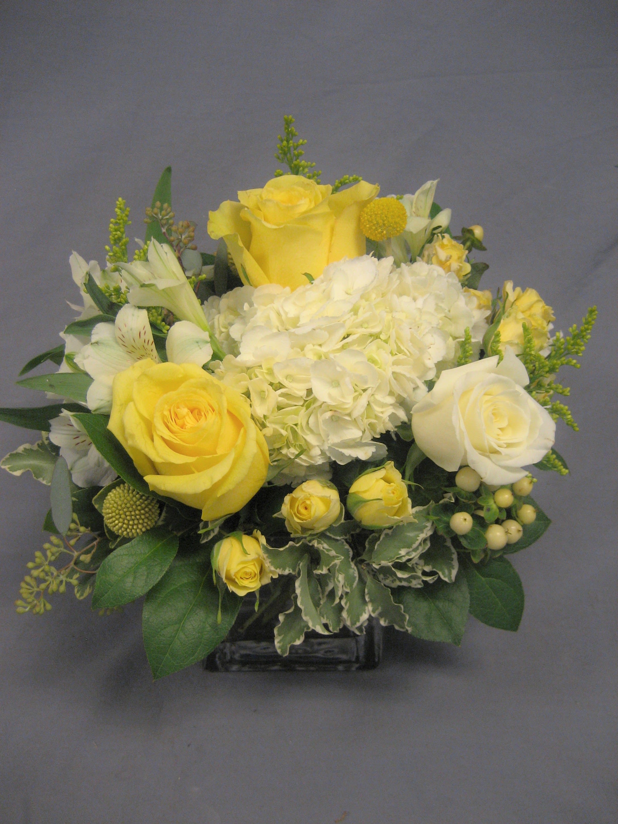 Sweetest Sunrise E69 - This sparkling array of sunny favorites in a cylinder vase will be the star of any room. It's a sweet gift she'll love to receive - and you'll be proud to give. The cheerful bouquet includes white and yellow flowers accented with fresh greenery. Upgrading to a Deluxe or Premium bouquet will add more flowers to the arrangement.