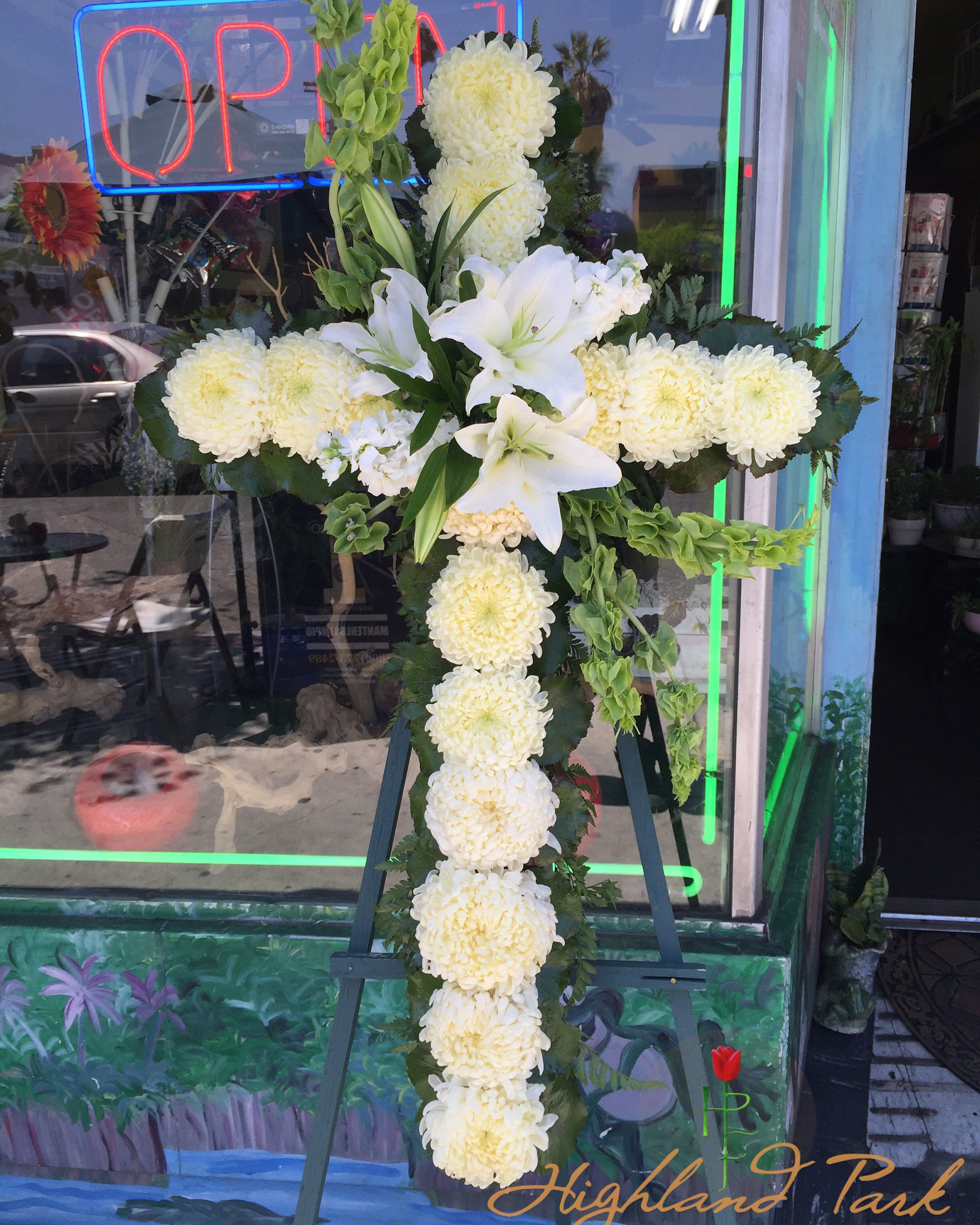 White floral cross arrangement on an easel with lilies and chrysanthemums