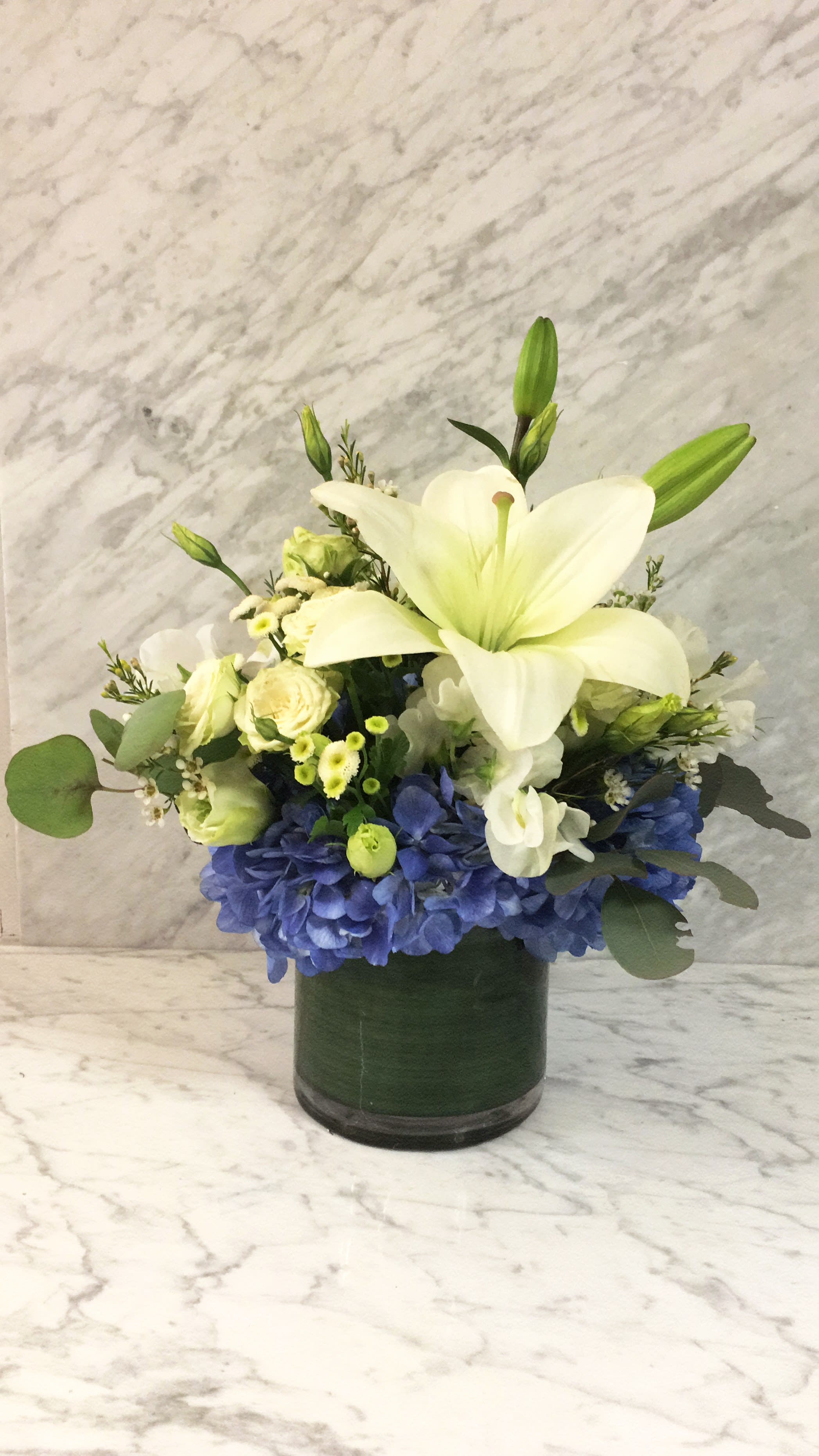 White lily and blue hydrangea arrangement in a dark glass vase