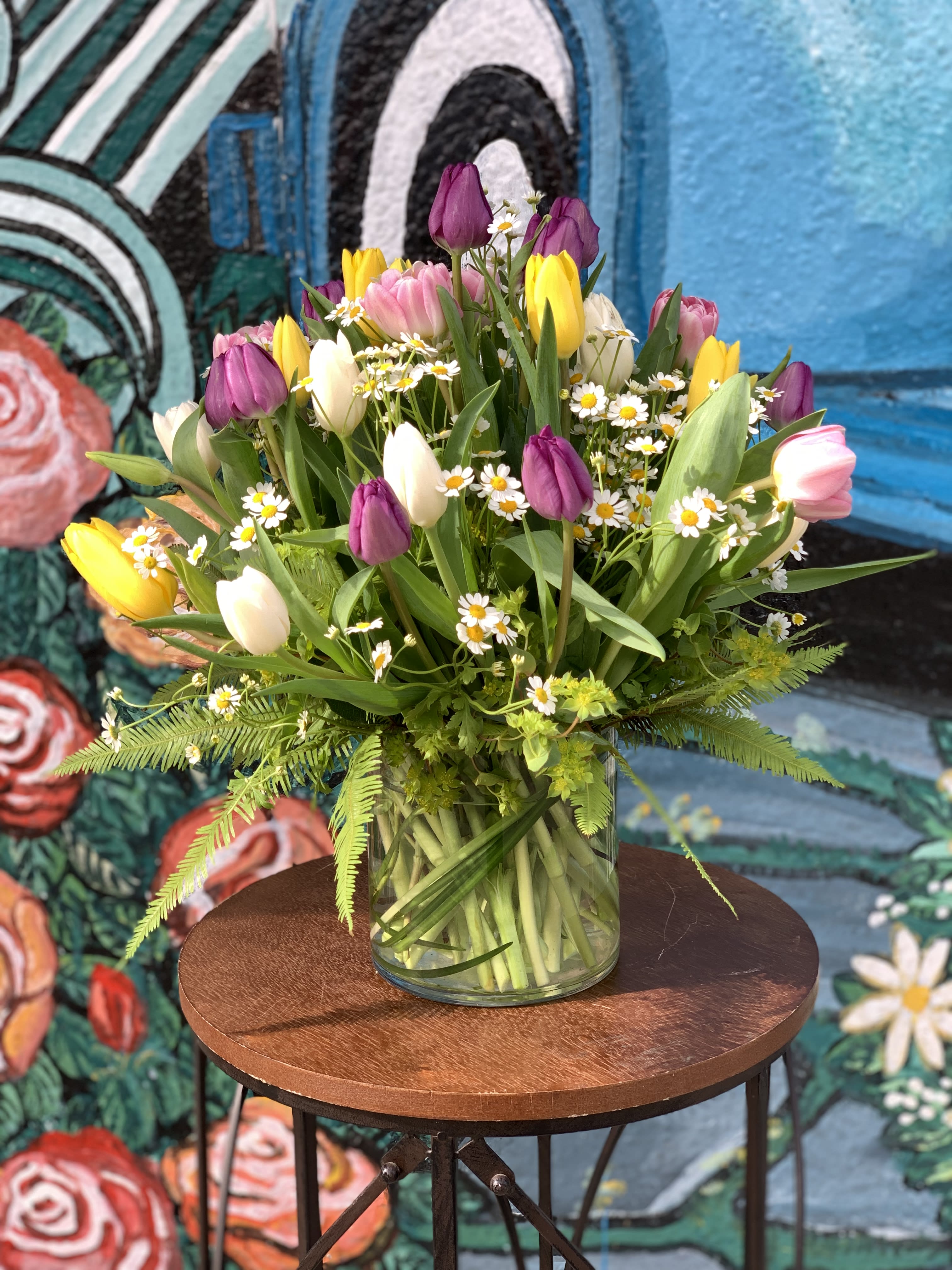 Mixed tulips and small white daisies in a clear glass vase