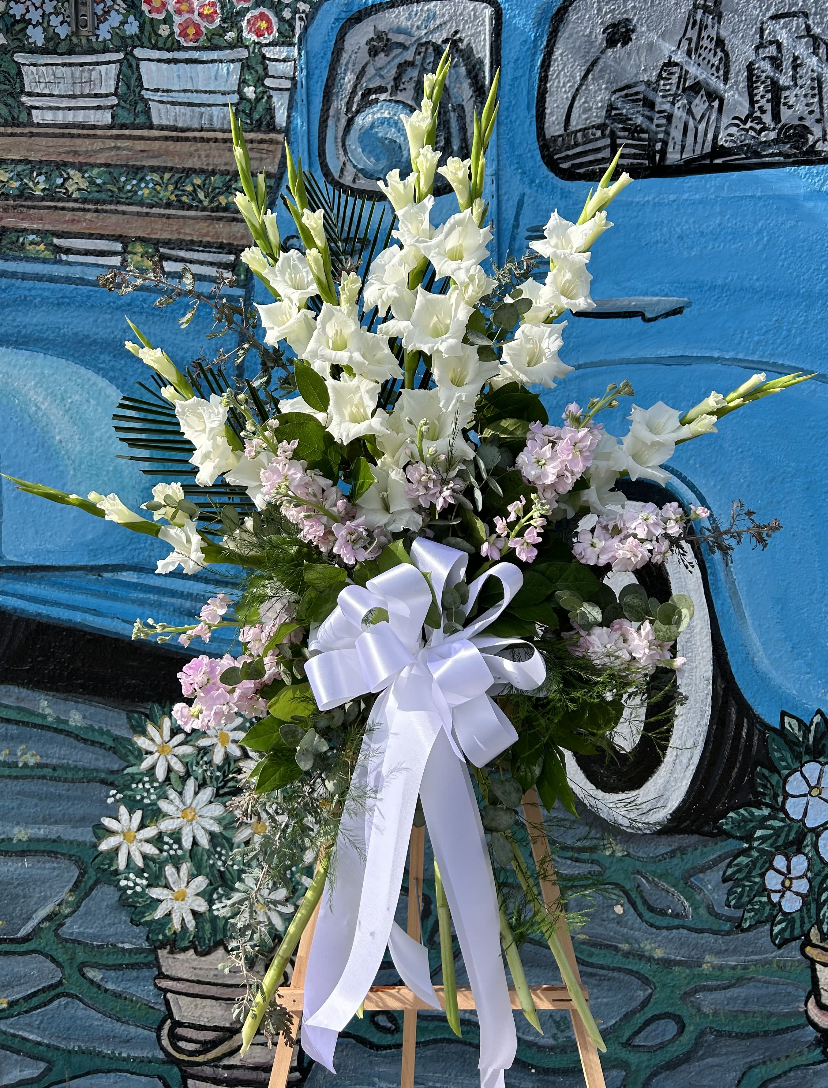 Tall white floral standing spray with a white ribbon on an easel