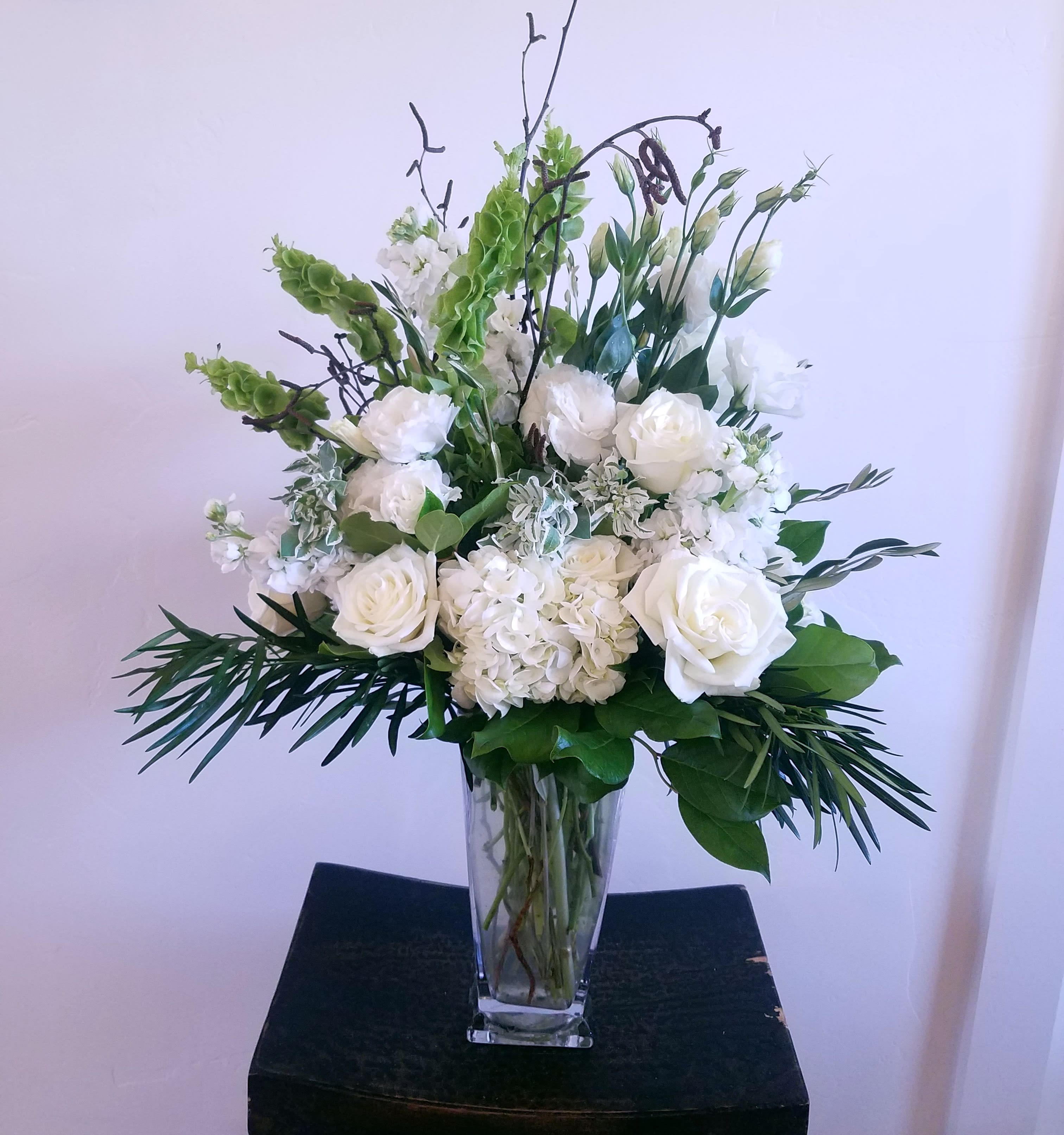 White floral arrangement in a clear glass vase with tall greenery