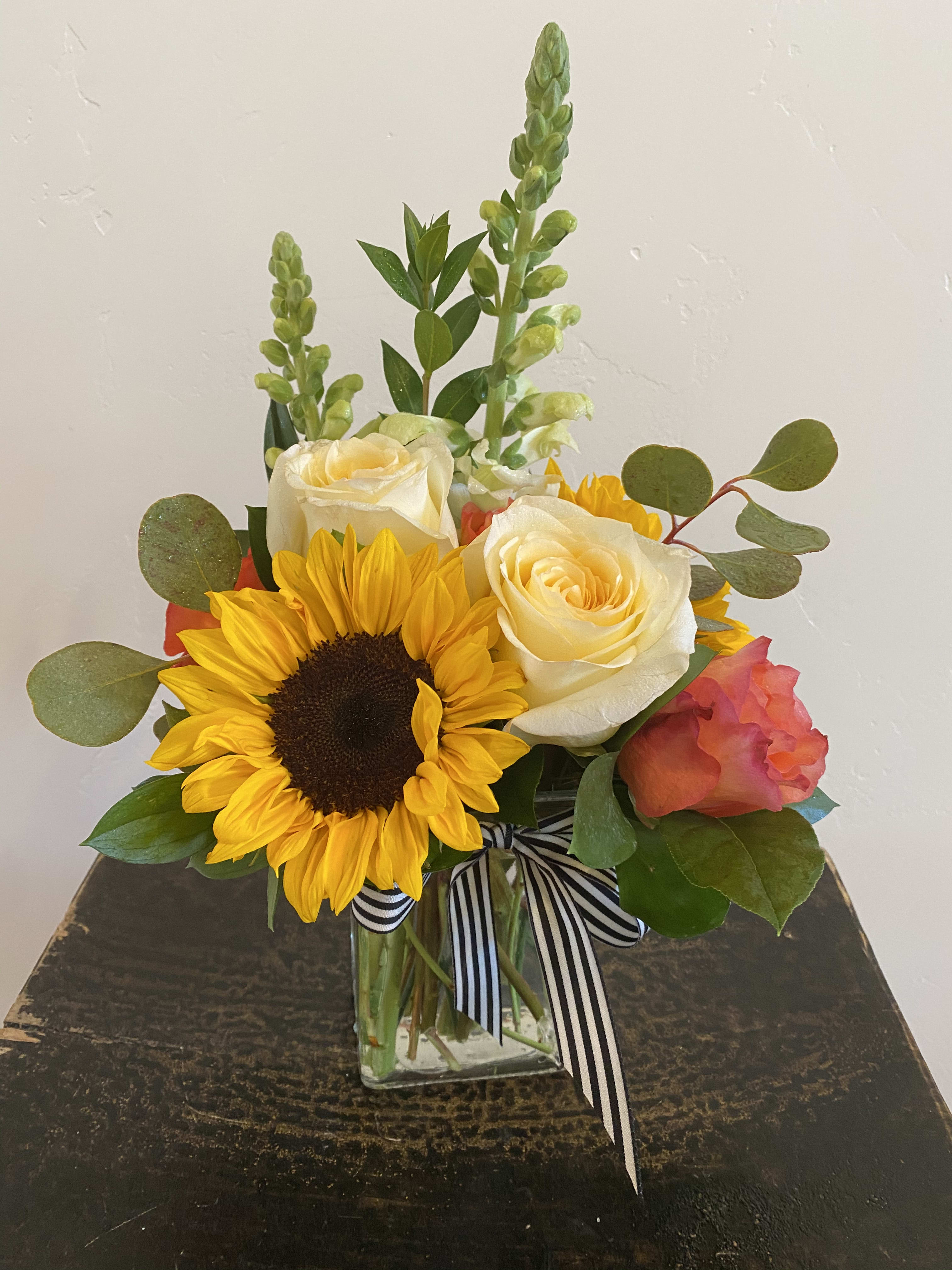 Sunflower and rose bouquet in a clear glass vase with striped ribbon