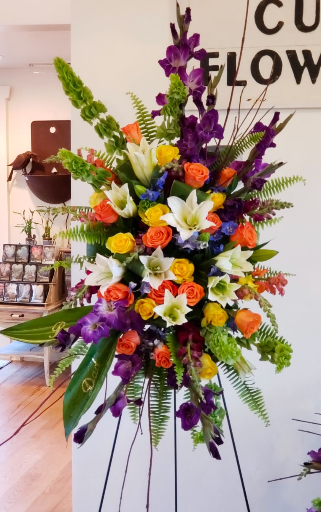 Tall standing spray of mixed roses, lilies, and purple flowers on an easel