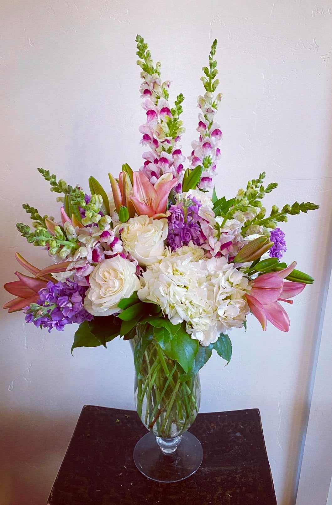 Tall bouquet of pink lilies, white roses, and purple flowers in a glass vase