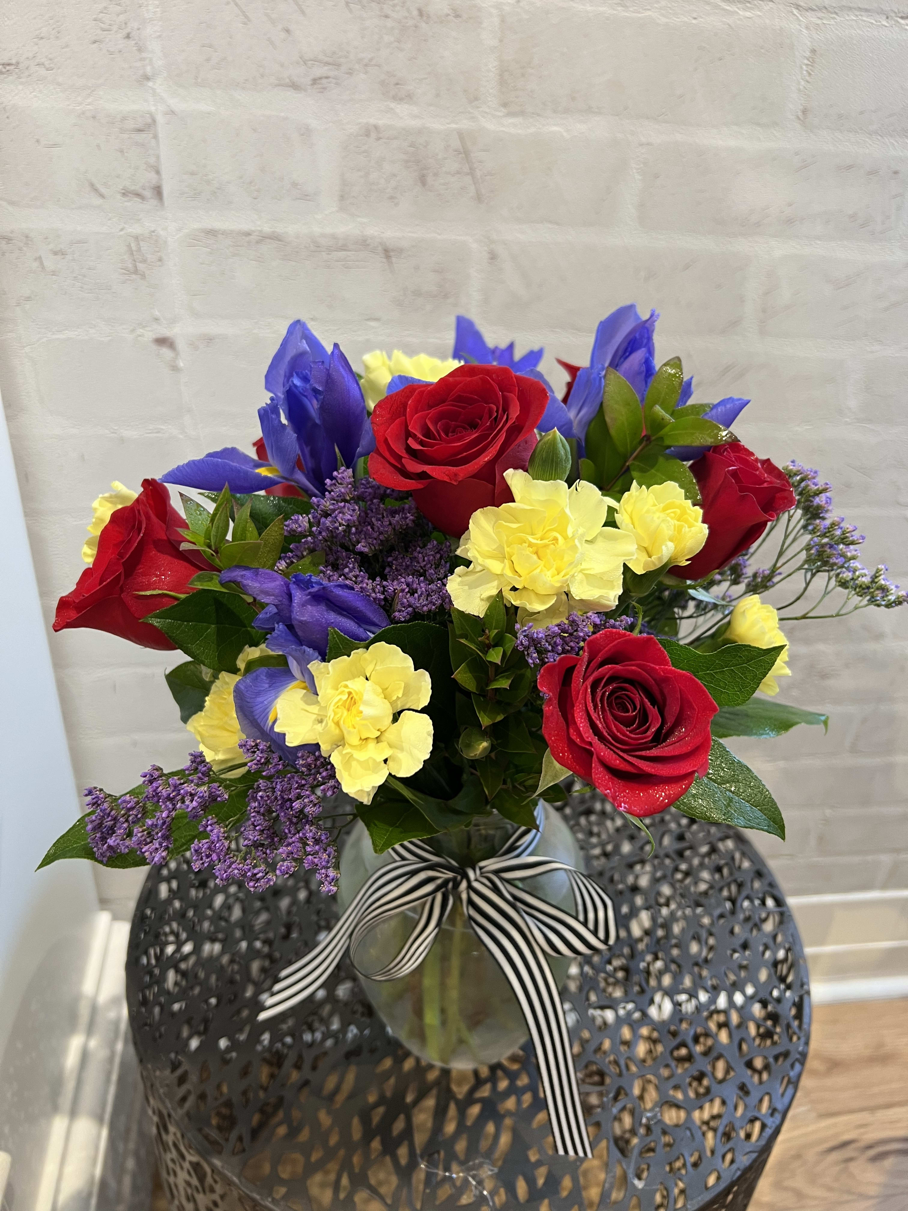 Bouquet of red roses, yellow carnations, and purple flowers in a glass vase