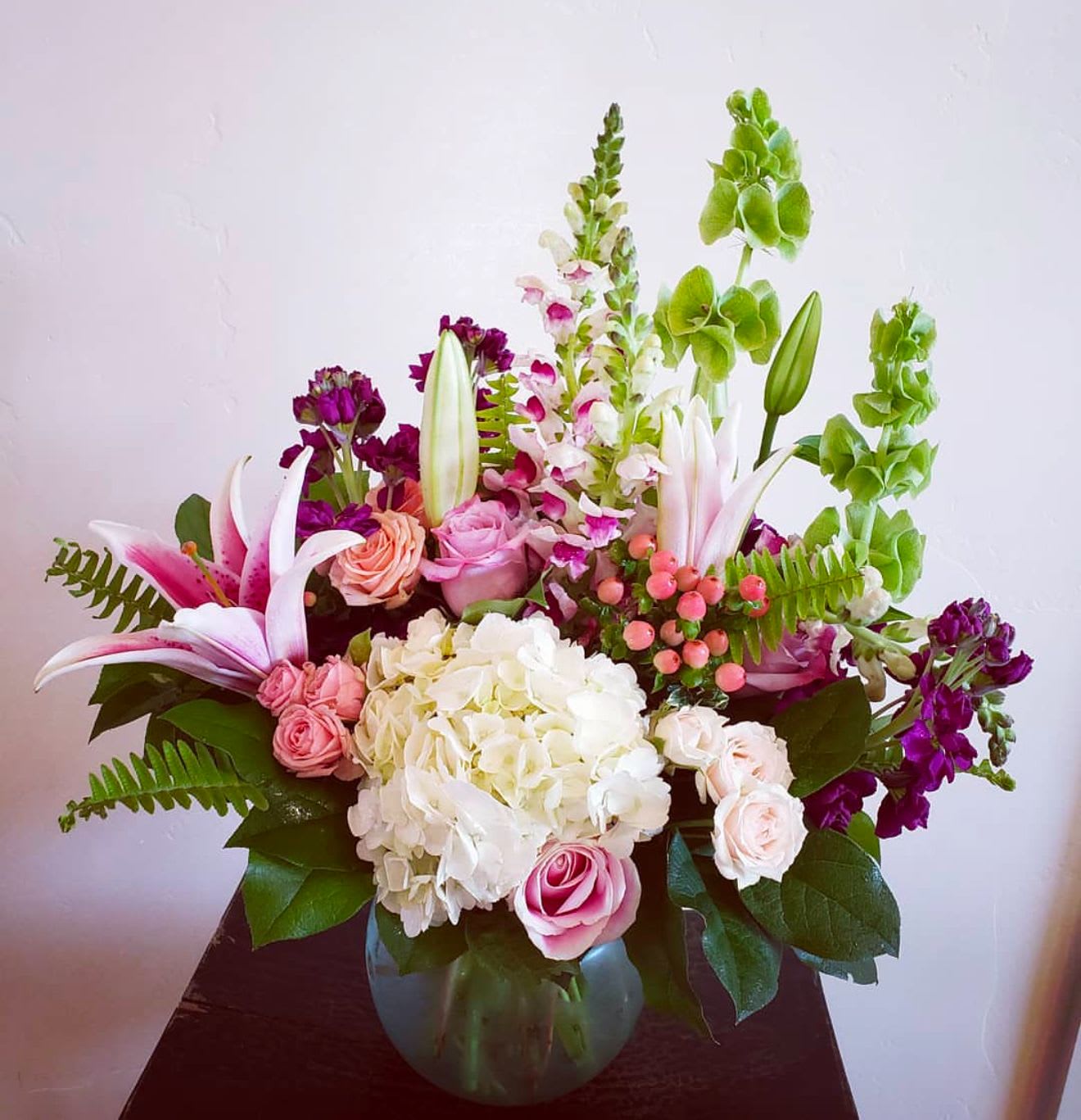 Mixed bouquet of pink lilies, roses, hydrangea, and snapdragons in a round glass vase