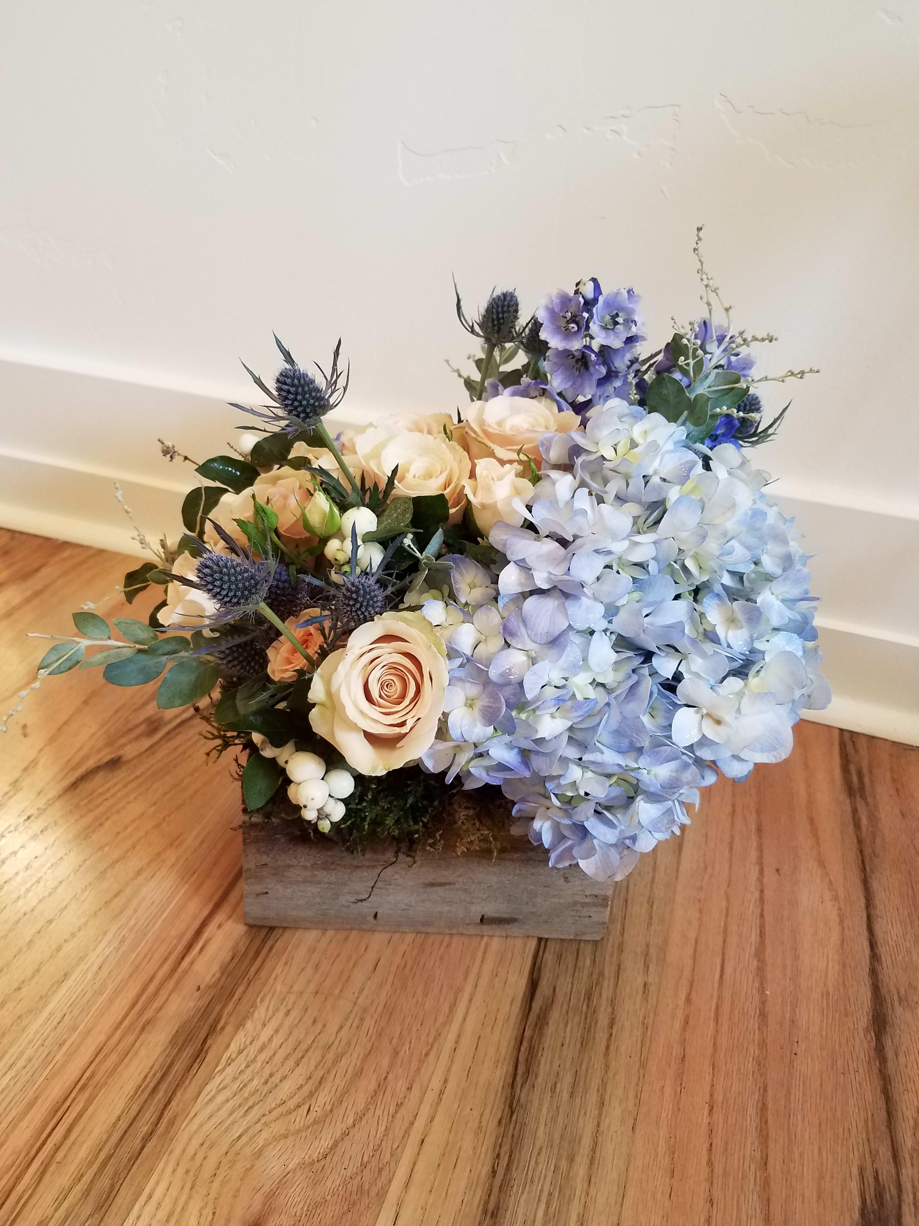 Low wood box arrangement with blue hydrangeas, peach roses, and blue accent flowers