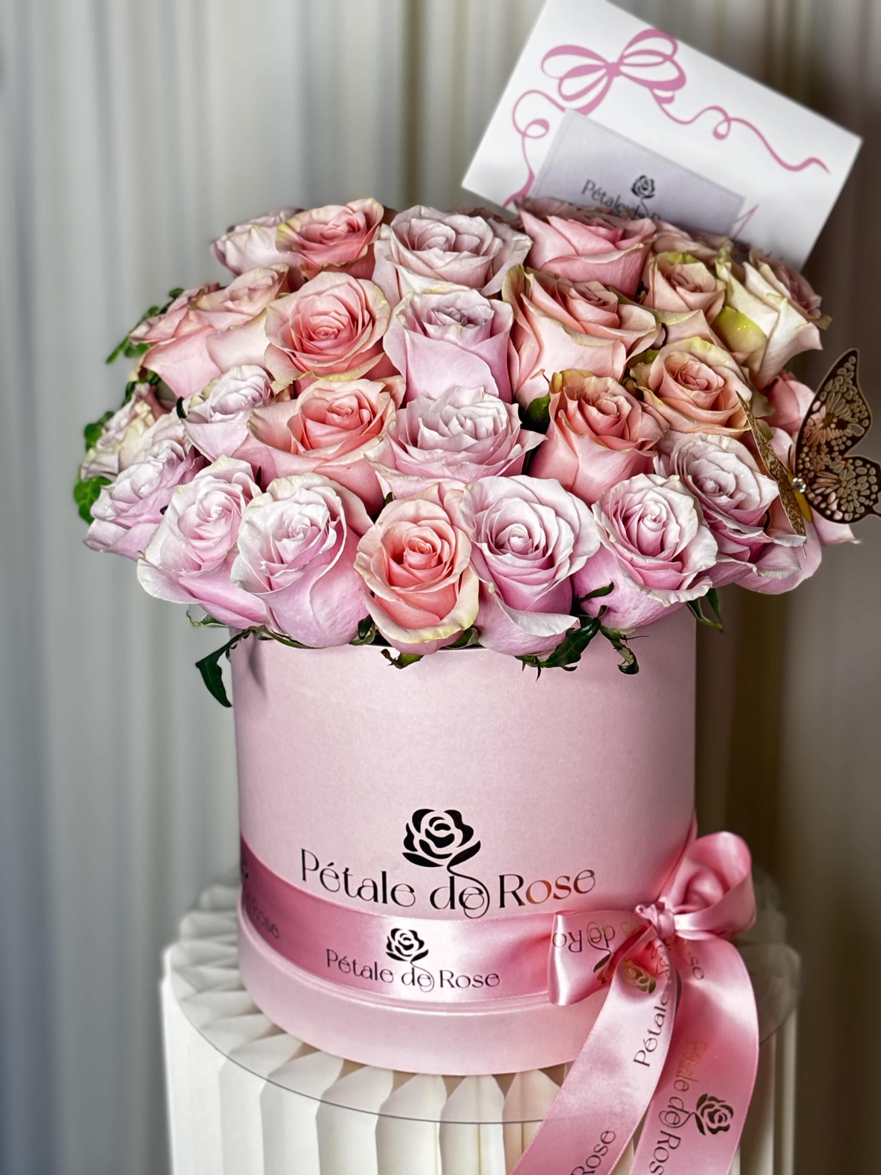 Pink and blush roses arranged in a round pink hat box with a ribbon bow.