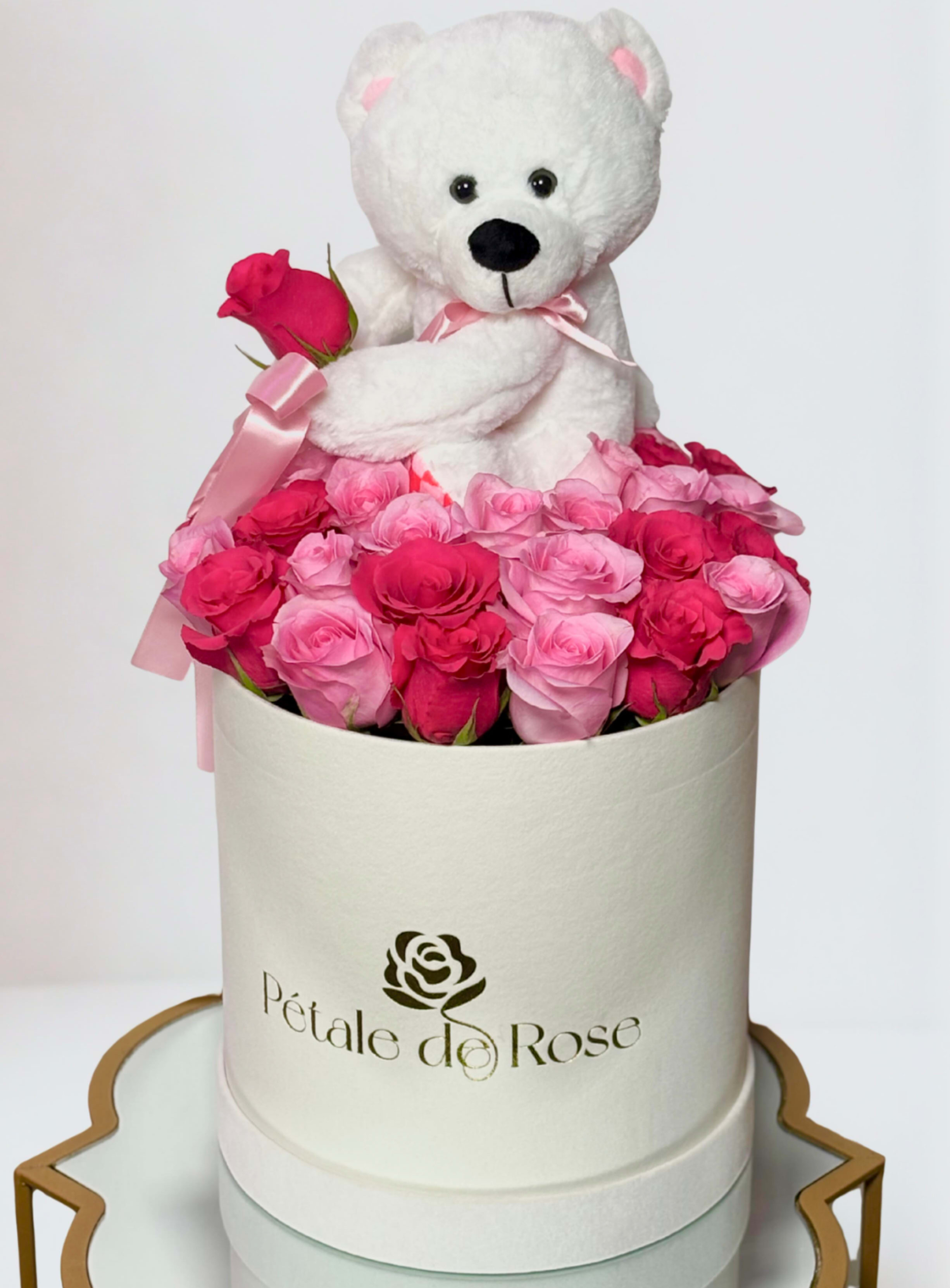 White teddy bear sitting in a box of pink roses with a ribbon