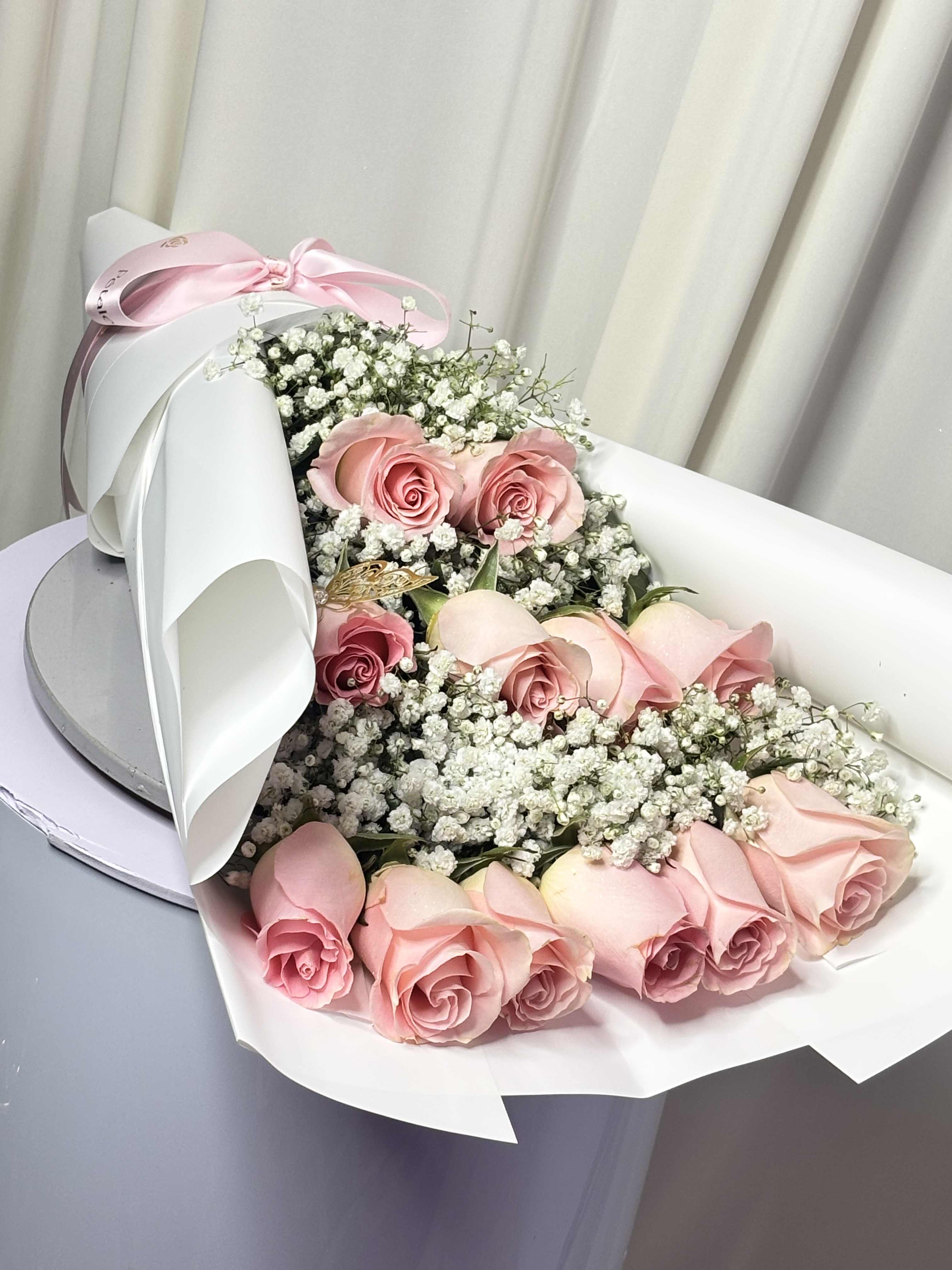 Pink roses with baby's breath in white wrapping and a pink ribbon
