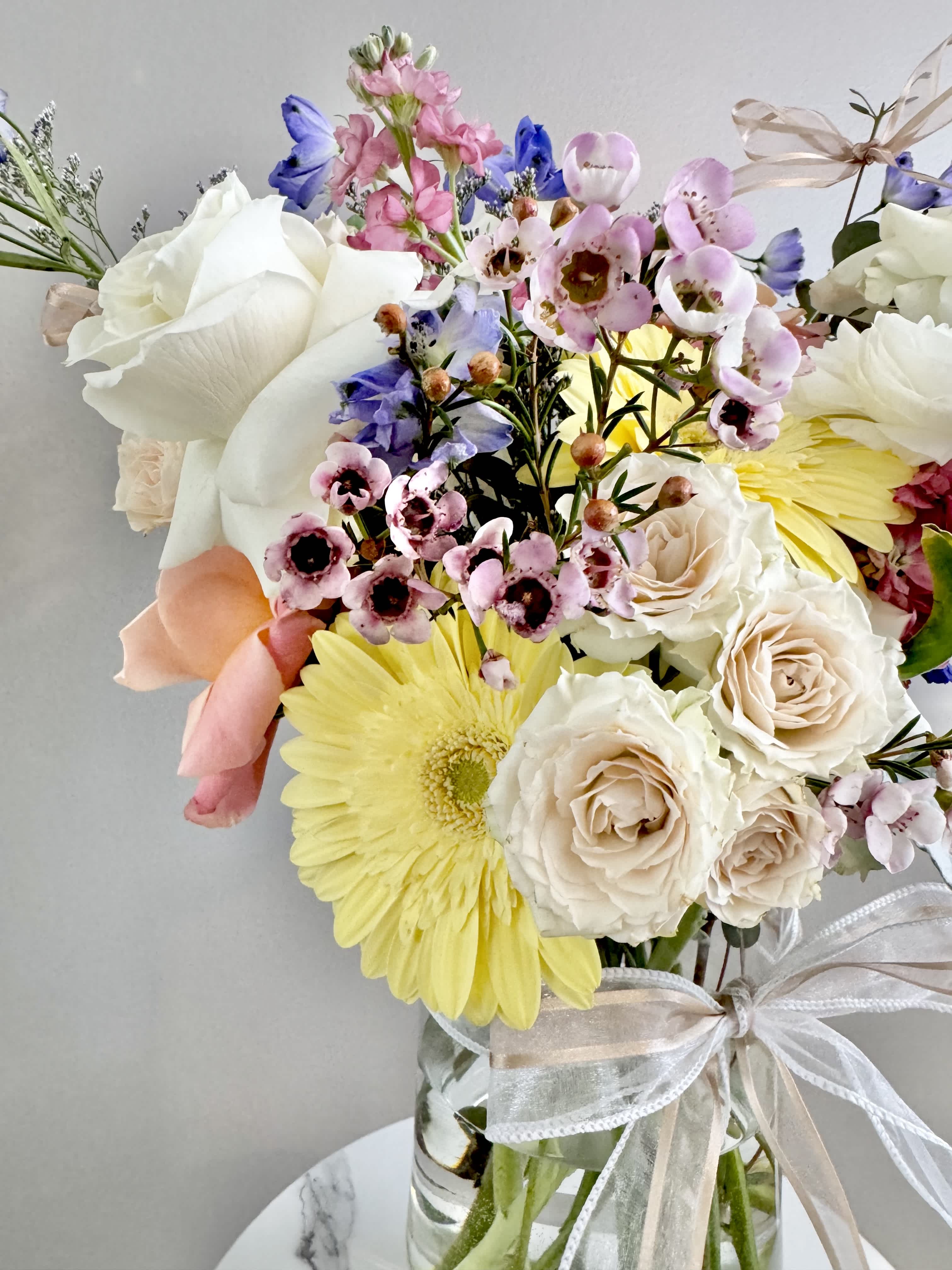 Mixed bouquet of roses, daisies, and pink blossoms in a glass vase with ribbon