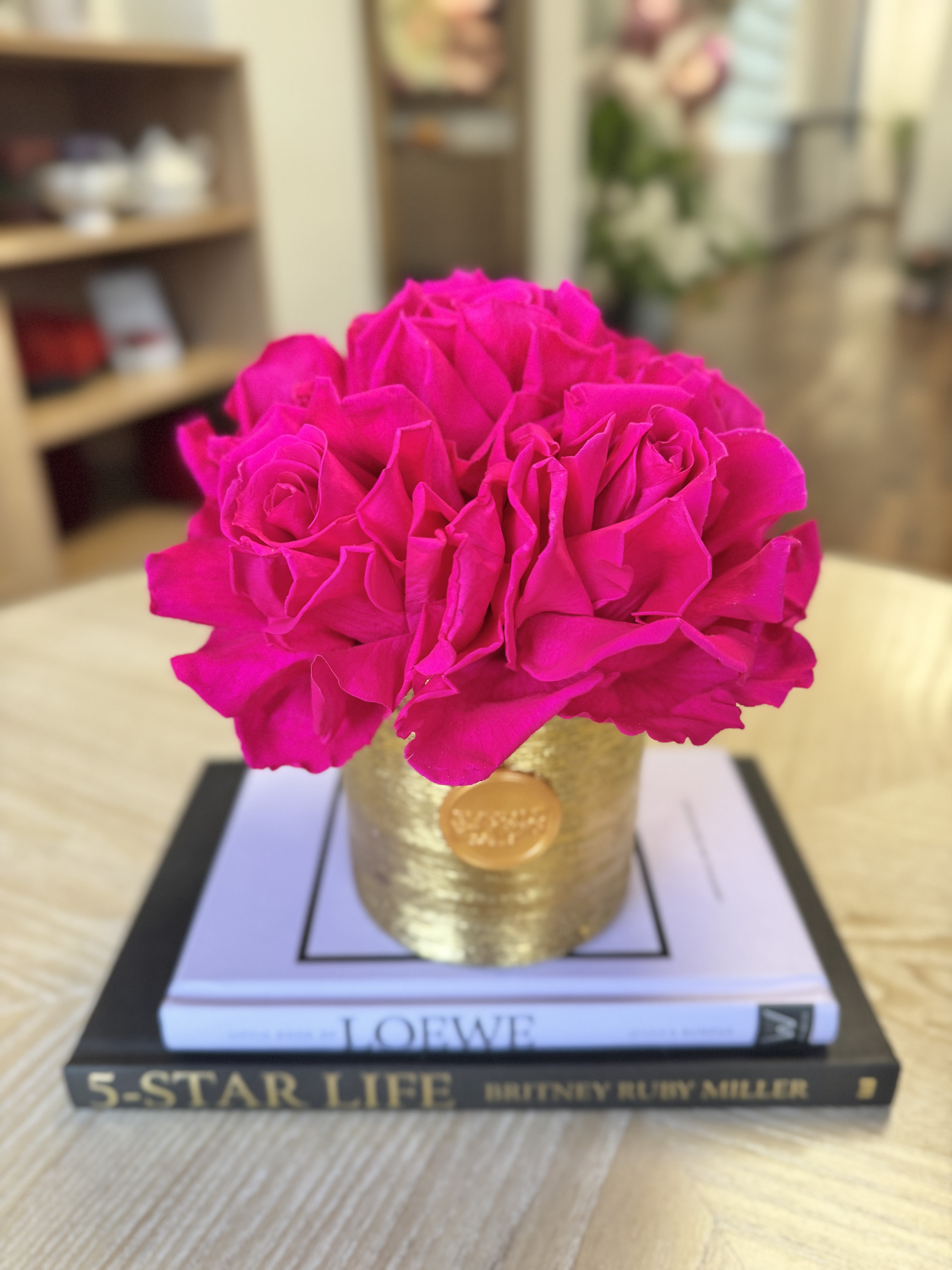 Bright pink roses arranged in a gold container on stacked books