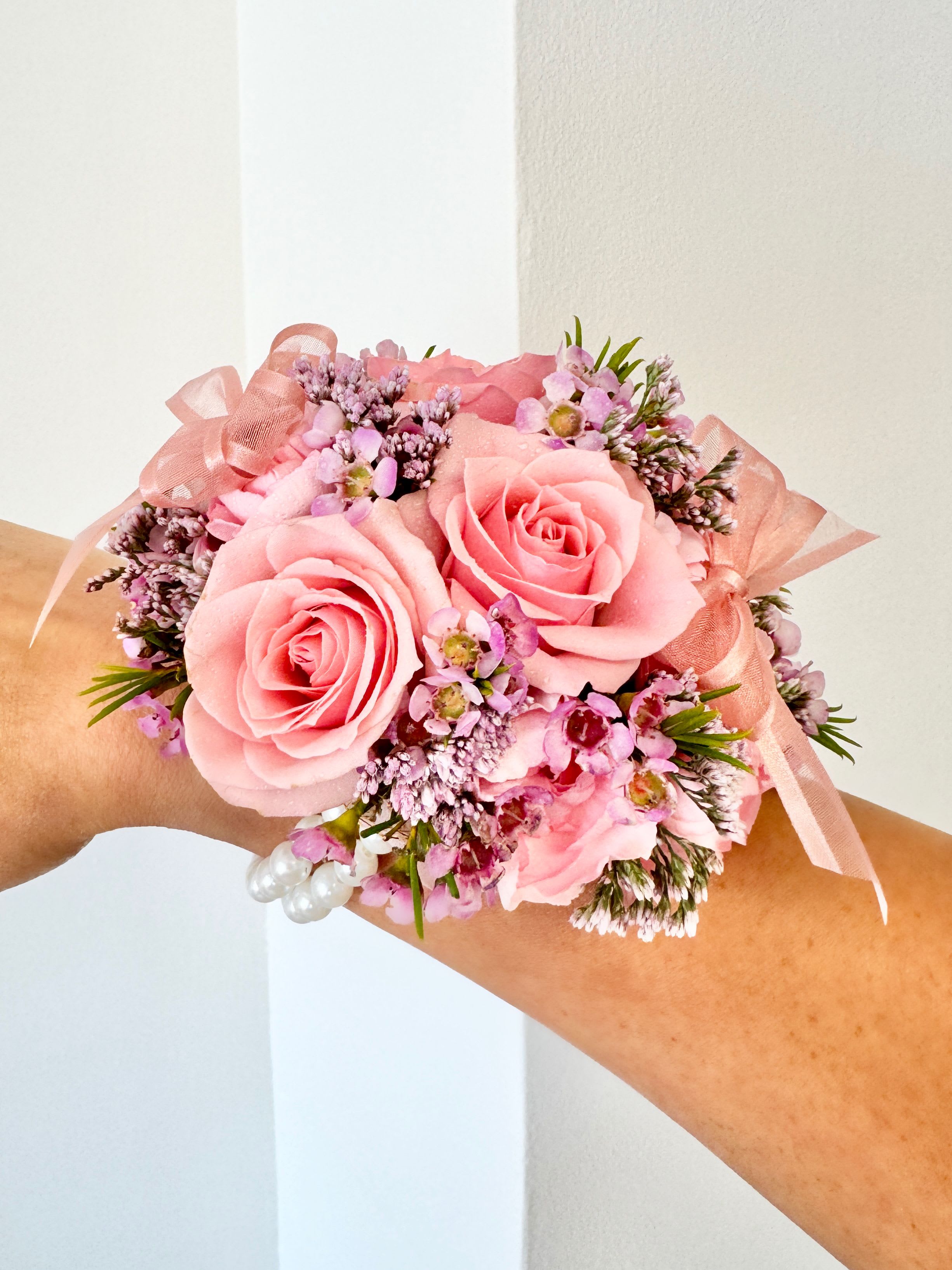 Corsage - A youthful and elegant design especially created by the Florist. Flowers are hand selected by the Florist. Perfect for prom, homecoming, and school dance.  Please specify preferred color theme in the Florist Instructions when ordering. Colors can be in White, Pink, Blue, Lavender, Orange, Red, Yellow, Green or No Preference.  Corsages come with 2 strings of pearls (as pictured).  We highly advise ordering at least 2 days in advance to ensure availability of supplies for the Color Selection.  If your event falls on a weekend, choose Friday delivery. Corsage will stay fresh for a few days if kept in a fridge. Delivered in a waterproof box with clear plastic lid.