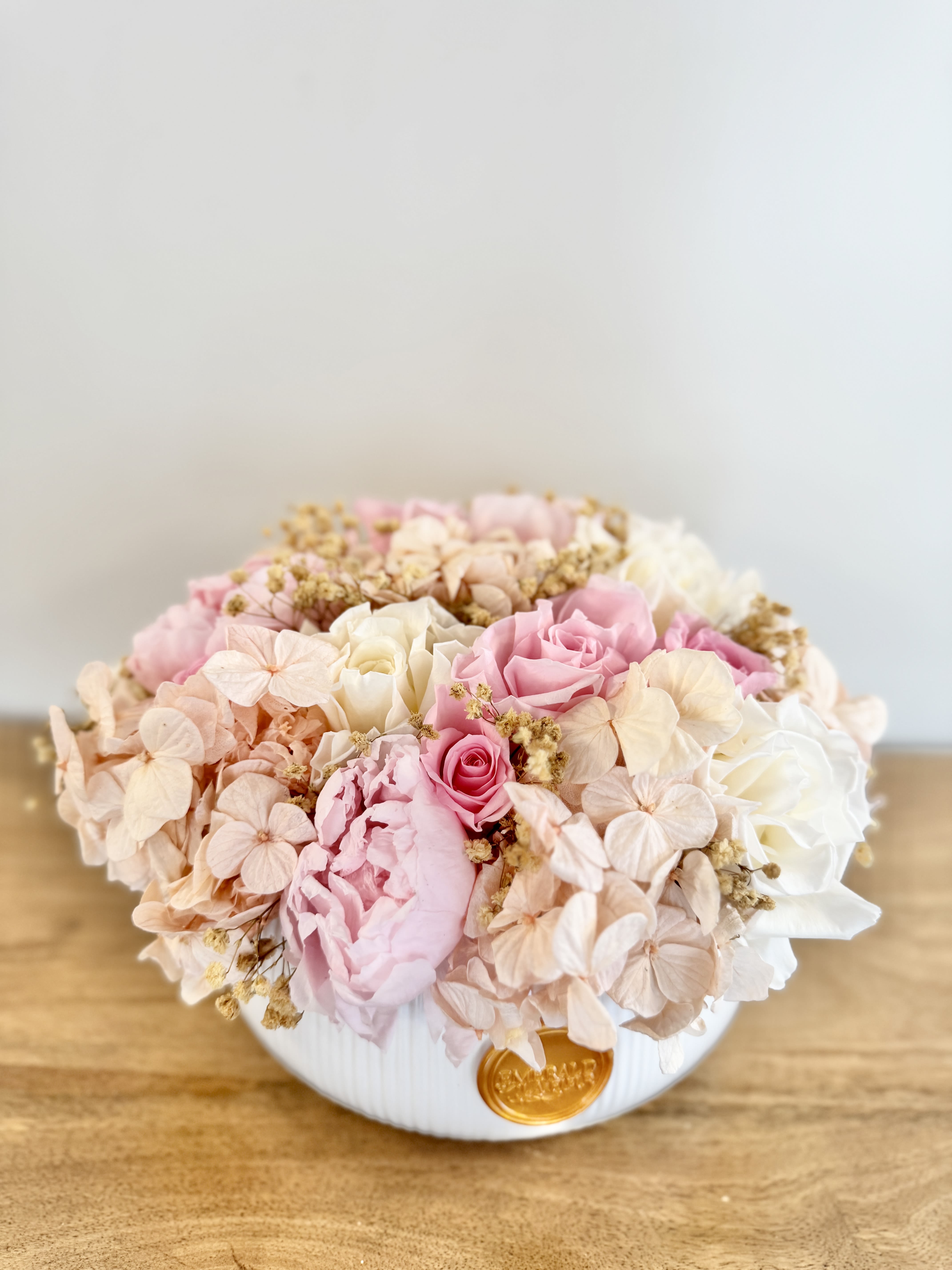 Eternelle Jardin – Blanc Luxe Classic - A timeless garden-inspired arrangement featuring premium preserved roses, hydrangeas, peonies, and delicate baby’s breath in soft ivory, blush, and champagne tones. Thoughtfully designed in our signature Blanc Luxe Classic vessel, Éternelle Jardin brings lasting beauty and refined elegance to any home or office. With proper care, this handcrafted arrangement can be enjoyed for months or even years, making it a meaningful gift and a luxurious décor piece.  Every Eternelle arrangement arrives beautifully presented in a premium gift box, making it the perfect choice for elevated gifting.  Care Tips: To preserve the beauty of your Eternelle arrangement, keep it in a cool, dry place away from direct sunlight, humidity, and heat sources. No watering or maintenance is required—simply enjoy its everlasting elegance. Avoid touching the roses frequently to maintain their delicate texture, and use a soft brush or gentle air duster to remove any dust from the petals or vase. With proper care, your arrangement will remain a stunning display of luxury for years to come.