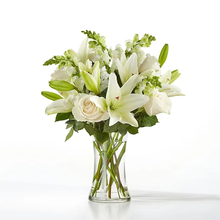 White lilies and roses arranged in a clear glass vase