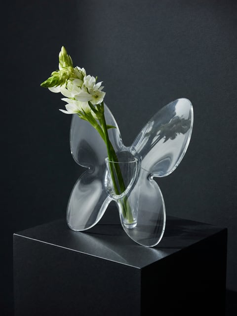 Acrylic Butterfly vase w/mini bouquet of blooms - A delicate cluster of white star-shaped blooms sits tucked into a clear butterfly-shaped glass vase for a gift that reads as thoughtful and modern. This flower arrangement for housewarming, just because, or birthday gently announces your sentiment without shouting-she'll feel seen by the quiet elegance and sculptural transparency of the vase, perfect for thinking-of-you moments, thank-yous, or a small anniversary gesture.  The bouquet features petite white flowers with green buds set inside a clear glass butterfly vessel; the transparent shape becomes the centerpiece, letting light play through stems for a clean, contemporary look. The piece pairs beautifully with tabletops, bedside dressers, or mantel displays alongside the included candle and bowl styling options shown-an easy, low-fuss accent that also suits get well, sympathy, wedding, or mother's day sentiments. Order sizes are compact and designed for everyday gifting; care is simple-fresh water every few days and a trim of stems as needed to keep the display looking crisp.