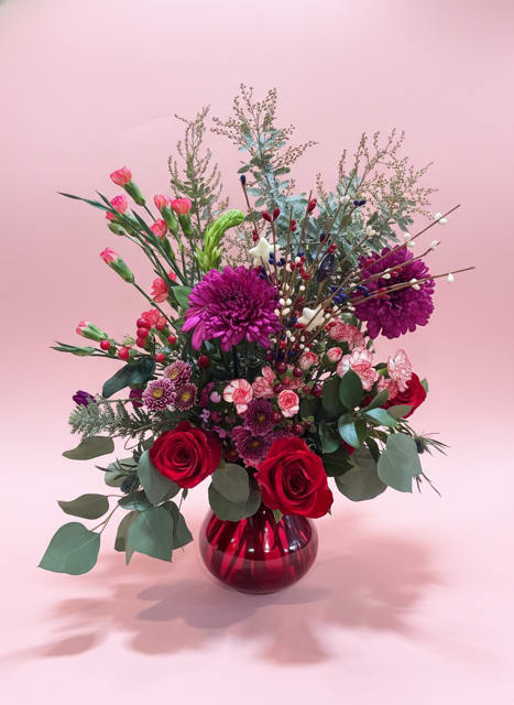 Burst of Stars Bouquet - Deep, romantic red roses meet vivid purple chrysanthemums and soft pink lisianthus in a bouquet that reads like a celebration-perfect as a birthday bouquet or a just-because arrangement to say "I'm thinking of you." The Burst of Stars Bouquet has a bold, layered palette of red, pink, purple and fresh green that creates instant warmth and a slightly festive look ideal for love and romance, thank-you gestures, housewarmings, or welcoming a new baby.  This flower arrangement mixes carnations, roses, chrysanthemums and lisianthus with airy eucalyptus-like foliage and tall branching accents for height and movement. Decorative berry stems add texture and a playful, twinkling detail, all arranged in a reflective red glass vase that anchors the composition and catches the light. The overall effect is full and luxurious without feeling fussy-a versatile centerpiece for summer gatherings, Fourth of July celebrations, weddings, or simply to make someone feel truly seen.