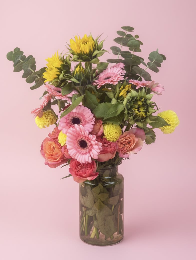 Gerber's in Sherbert - A burst of sherbet colors-peachy-pink gerbera daisies, coral and pink roses, and bright yellow chrysanthemums-creates an airy, upbeat bouquet that instantly lifts the room. This flower arrangement for birthdays, thank-you gestures, new baby celebrations, or just because moments reads like a cheerful garden in a clear glass vase; tall eucalyptus stems give height and a soft, natural texture so the recipient feels genuinely seen and celebrated.  The loose, upright composition is intentionally casual and hand‑arranged: layered blooms in pink, orange, peach and yellow sit above visible stems in a clear glass vase for a fresh, modern look. Expect lively movement and a mix of textures from smooth rose petals to daisy centers and feathery eucalyptus-perfect for spring, graduation, retirement, get-well, or thinking-of-you occasions. Vase dimensions and care: keep water fresh, recut stems if needed, and this bright mixed bouquet will bring sunny color to any room.