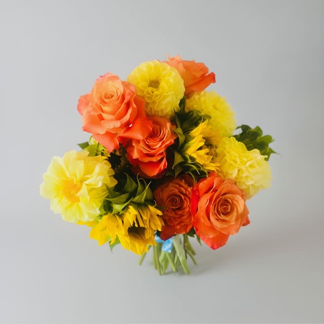 Golden Momentum - Sunburst warmth greets the eye in this compact hand-tied flower arrangement-bright orange roses and round yellow dahlias clustered into a full, rounded bouquet that feels like a sunny moment wrapped in stems. As a birthday bouquet, anniversary gift, Father's Day surprise, or just-because pick-me-up, Golden Momentum reads as cheerful and energetic; its saturated orange and yellow palette carries a hint of autumnal richness while staying perfectly at home in spring and summer celebrations.  The tightly gathered stems are finished in a simple bouquet wrap for easy handing and display; no vase needed unless you want to showcase the blooms on a table. Dahlias lend plush, geometric texture beside velvety roses, giving the arrangement a bold contrast and a lively, tactile presence. Ideal for thank-you gestures, congratulations, graduations, get-well wishes, retirements, or as a warm wedding or Mother's Day accent, this bouquet is designed to make the person you're thinking of feel genuinely seen and celebrated.