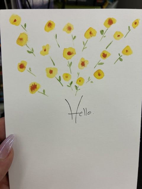 Hello w/flowers card - A cluster of delicate yellow blooms with warm orange-red centers crowns the top of this handmade greeting card, evoking sunlit gardens and easy summer afternoons. The thin green stems and airy composition pair with a casually handwritten "Hello" across the lower half, making this card ideal as a birthday note, a thinking-of-you message, or a simple just-because hello that brightens someone's day.  Made with a clean, understated design and room to write your own message, the card arrives ready for a personal, handwritten sentiment. Its cheerful white, yellow, green, and orange palette reads fresh for spring and summer and also works beautifully as a thank-you or Mother's Day note-small, sincere, and effortlessly charming for the person you're thinking of.