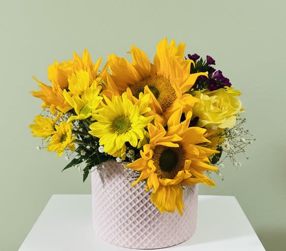 Mellow Yellow bouquet - A burst of sunny cheer-this Mellow Yellow bouquet pairs bold yellow sunflowers and daisy-like blooms with soft pinks, whites, and tiny purple accents to create an uplifting birthday or thank-you gift. Designed for occasions from Spring and Summer celebrations to Get Well wishes, Thinking of You moments, Father's Day, or a bright housewarming present, it reads as casual, joyful, and effortlessly optimistic for the person you're celebrating.  The stems are gathered in a pale pink,custom ceramic vase that adds tactile contrast and a modern, home-ready accent to the vivid petals. Alongside sunflowers you'll find cheerful daisies, mixed carnations and seasonal filler for a full, dense look that feels fresh and informal. Sizes and exact flower count vary seasonally to ensure peak freshness; simple care-fresh water every other day and a cool spot away from direct sun-keeps the arrangement looking its best.