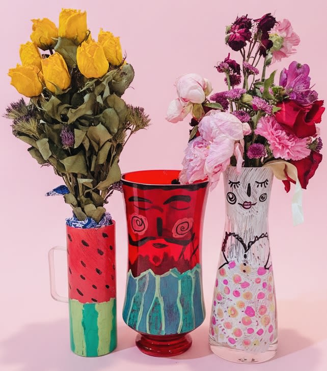 Painted pairs "Mamasita with macho melon man" vases w/a gift bouquet inside - Three playful painted vessels hold a trio of cheerful bouquets designed to make someone feel seen-perfect as a Just Because, Thank You, Thinking of You, or lighthearted Birthday gift. This flower arrangement set pairs a painted glass mug, vase, and bottle (each with whimsical hand-painted faces and patterns) with a mix of yellow, white, purple, pink, and red blooms to create a bright, arts-and-crafts look that's equally fitting for Spring, Summer, or an informal wedding accent. The casual, handmade vibe also makes it a fun Father's Day surprise or a colorful addition to a Valentine's or Mother's Day gift set.  Each small bouquet combines roses and carnations with complementary seasonal stems for texture and variety: one vessel centers on sunny yellow roses, another on vivid red blooms, and the third blends pink, purple, deep red, and white florals for a playful, layered palette. The painted glass mug, vase, and bottle come tied with ribbon and work as keepsake containers after the flowers fade, adding lasting charm to the recipient's desk or kitchen windowsill.  Give this set to the person who appreciates handcrafted details and joyful color-the kind of arrangement that makes them smile the moment they see it. These petite arrangements are ready to present as a coordinated gift set; simple care-fresh water every couple of days and a cool spot out of direct midday sun-will keep the flowers looking their best.
